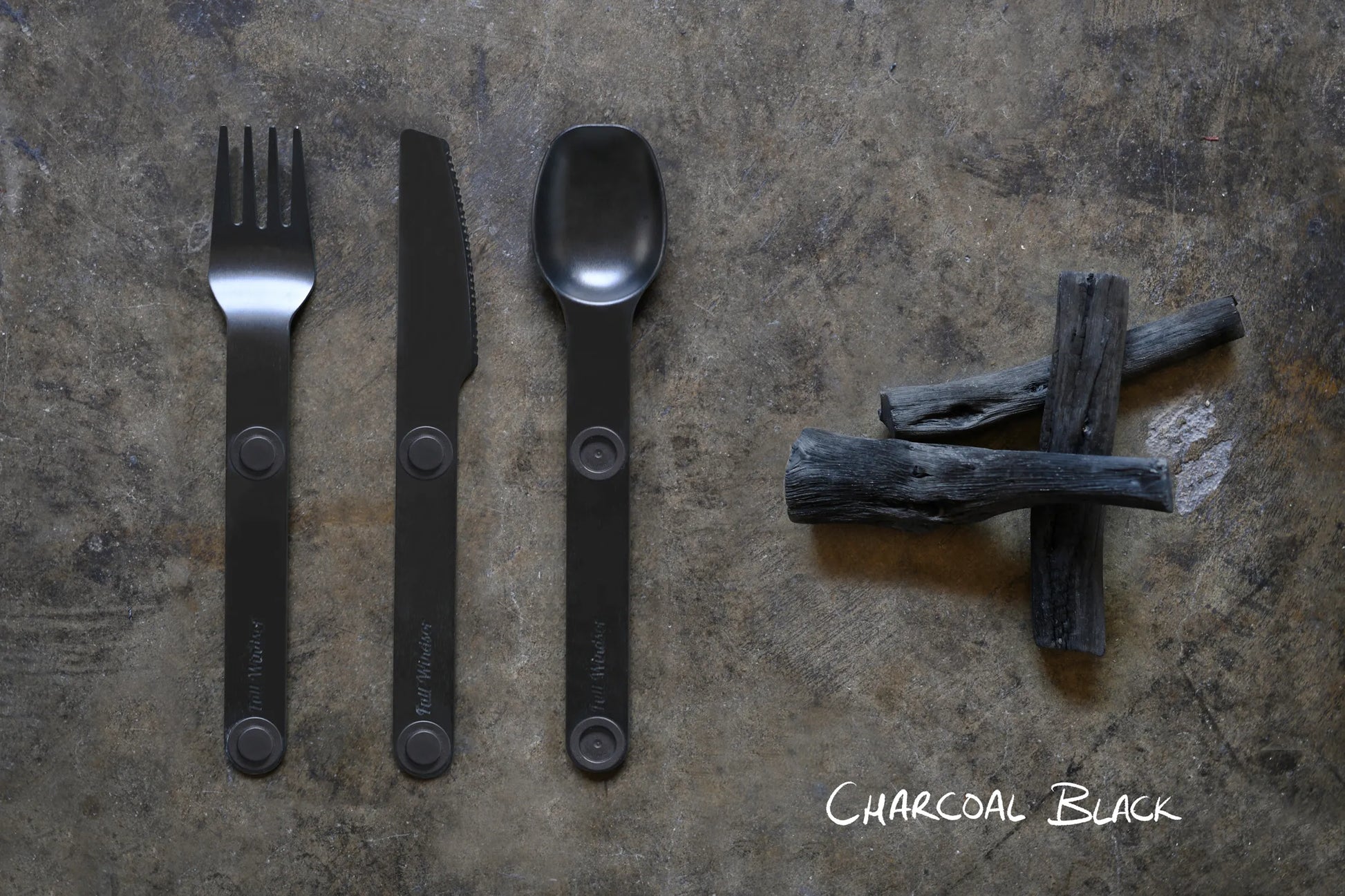 Black fork, spoon and knife next to charcoal.