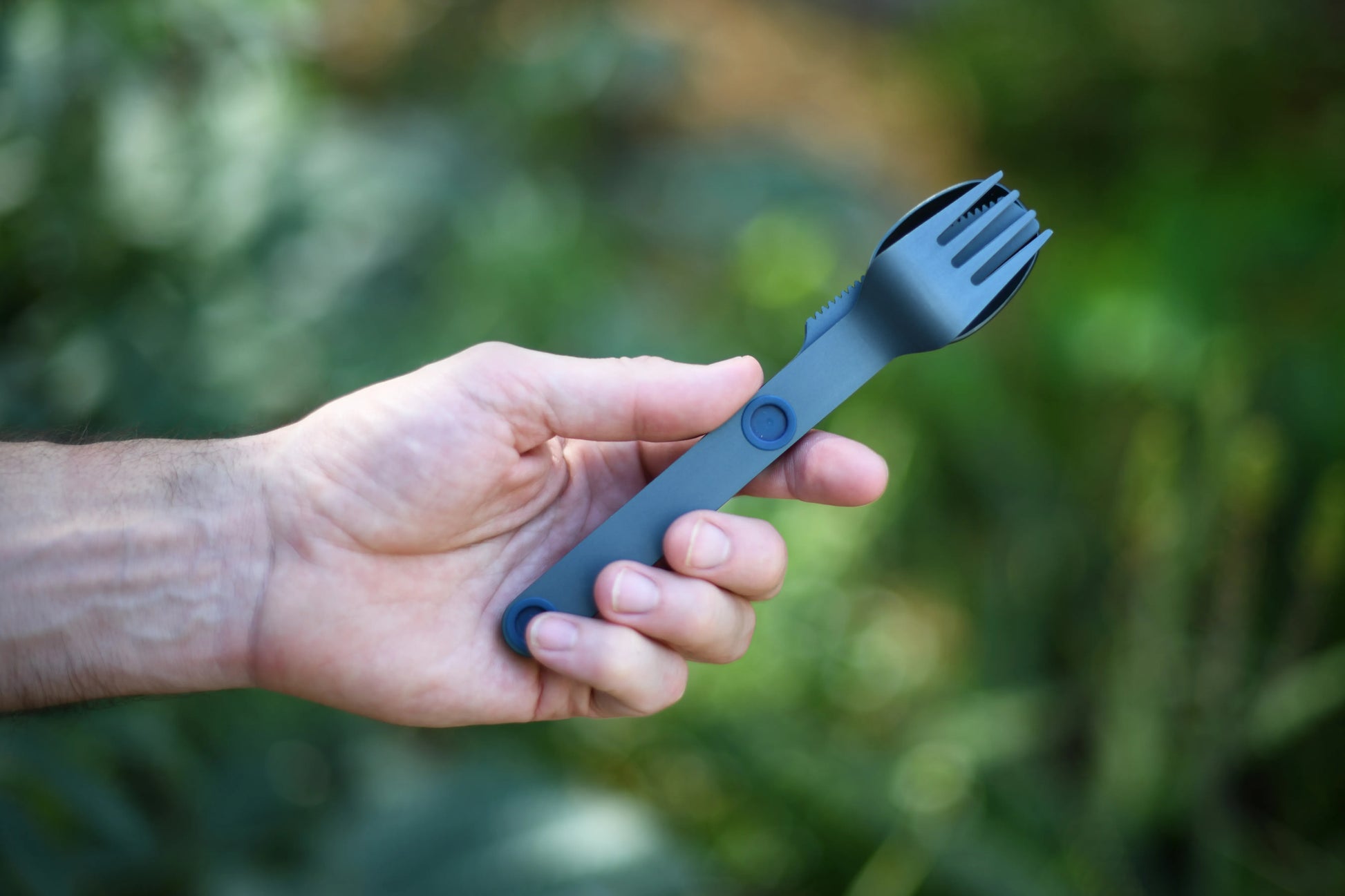 Hand holding a blue fork, spoon and knife connected.