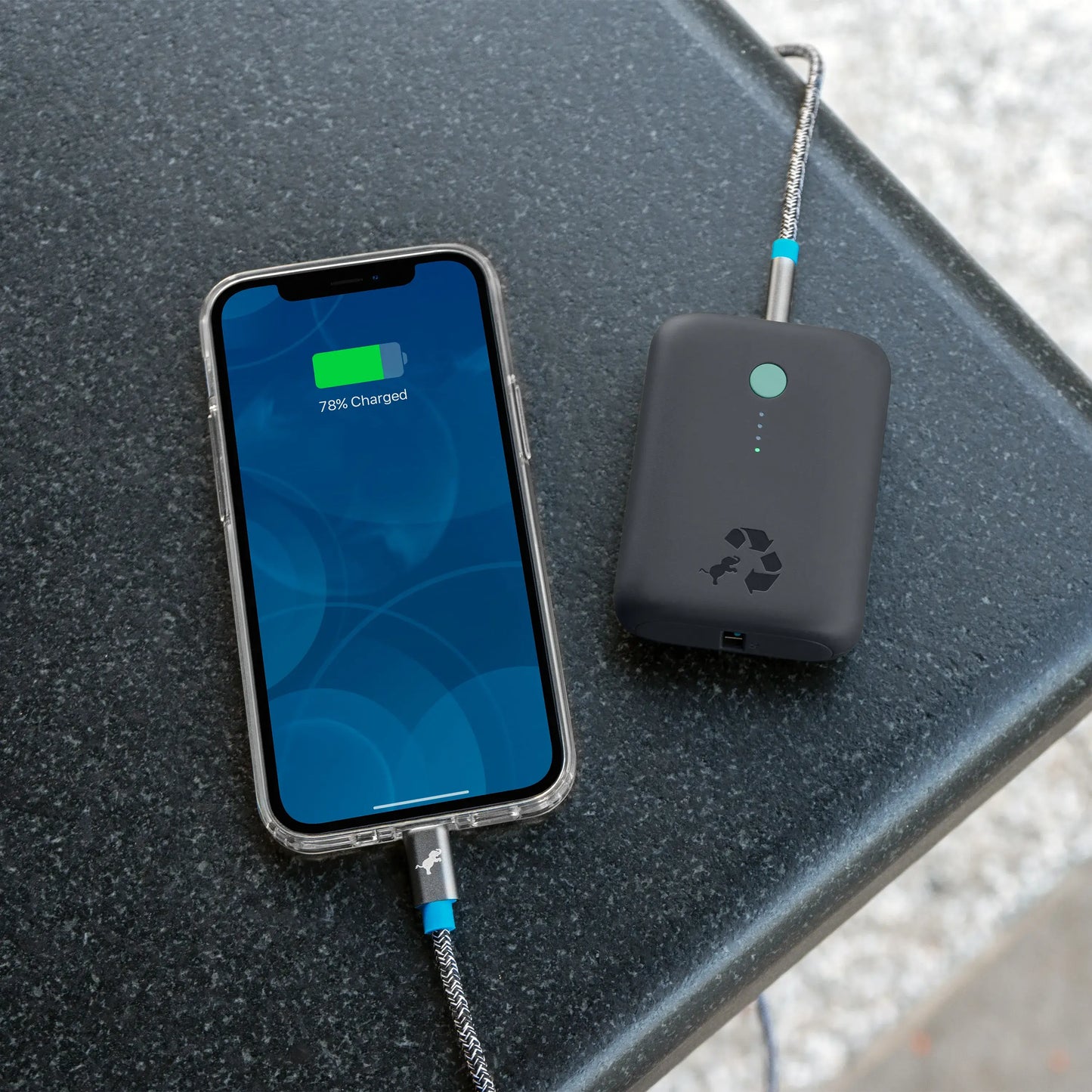 Charcoal portable charger with green button connected to cell phone on countertop.