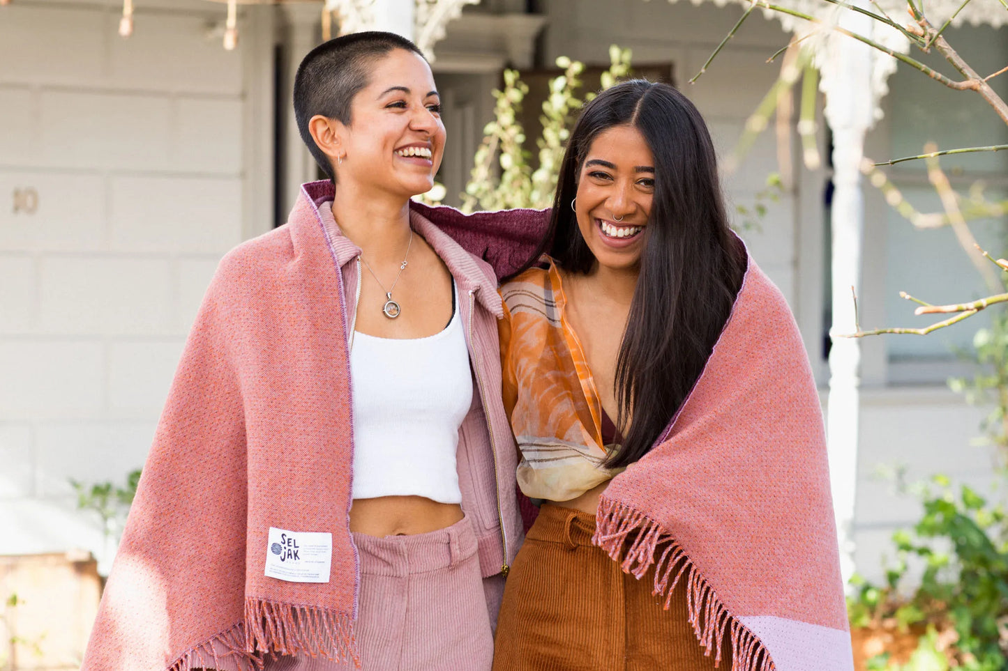 Two women laughing and wearing a red and pink wool blanket.