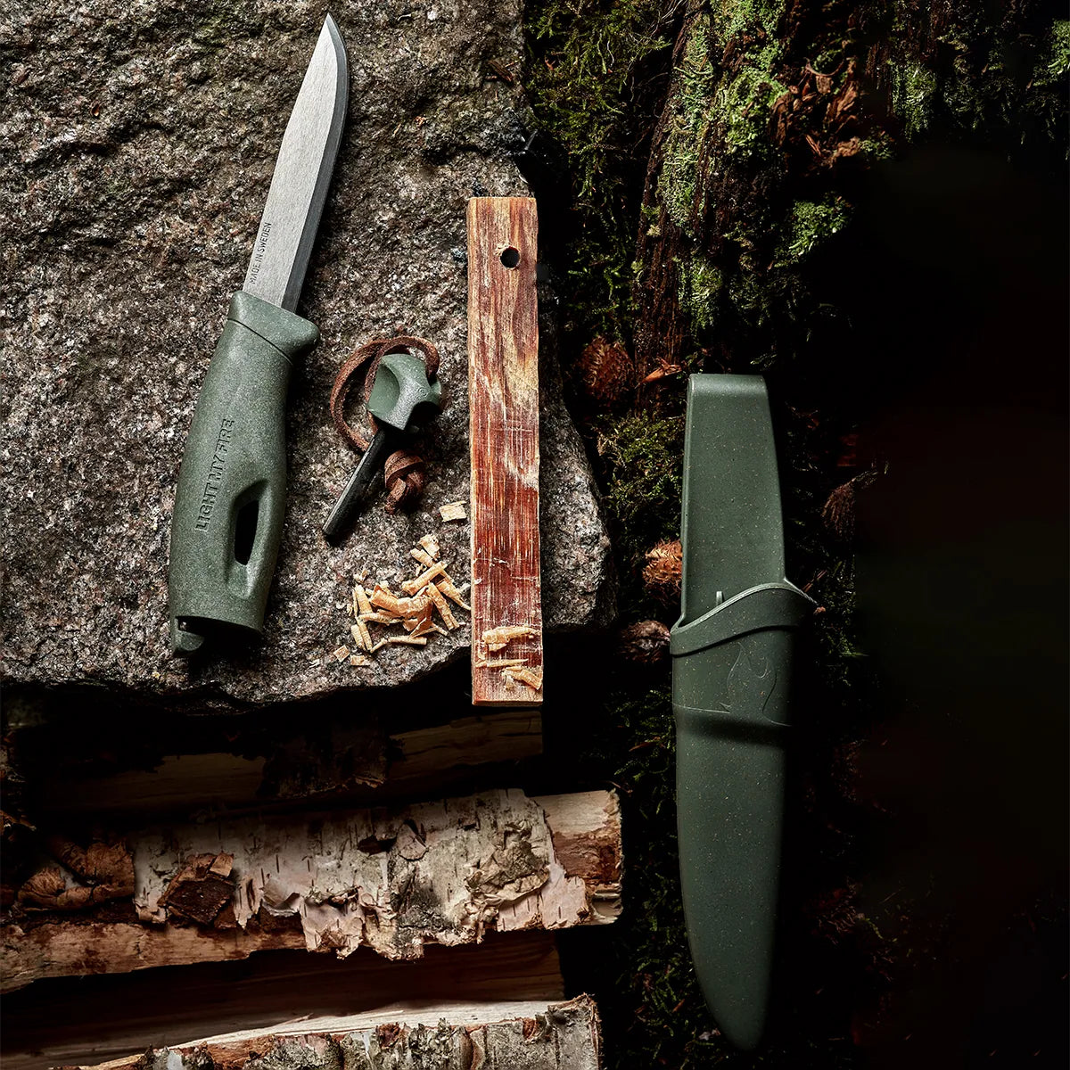 Green knife and sheath on a rock next to wood.