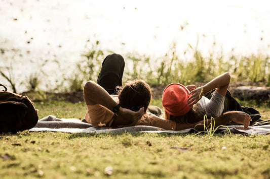 Man and woman lying on a blanket outside by a lake.