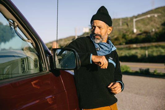 Man outside wearing a bandana leaning against a car.