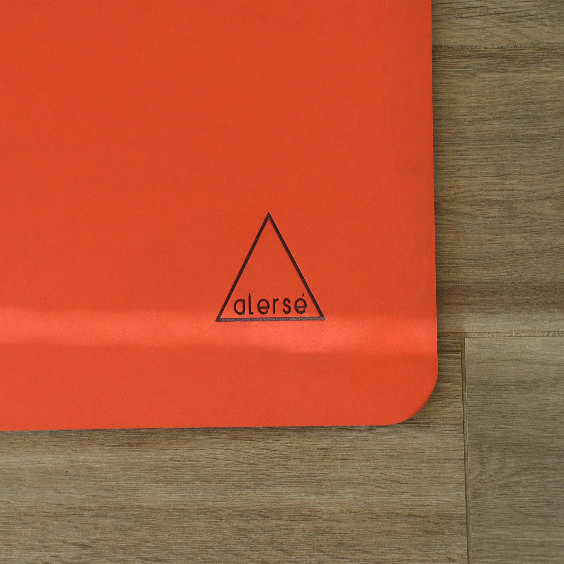 Corner of a red yoga mat with a Alerse logo on it.
