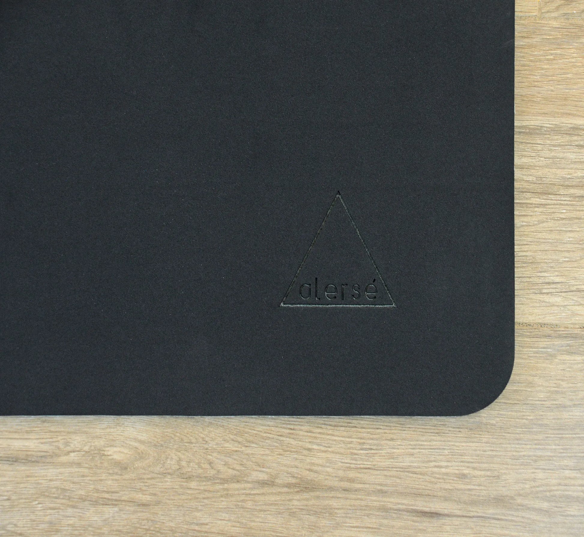 Corner of a black yoga mat with a Alerse logo on it.