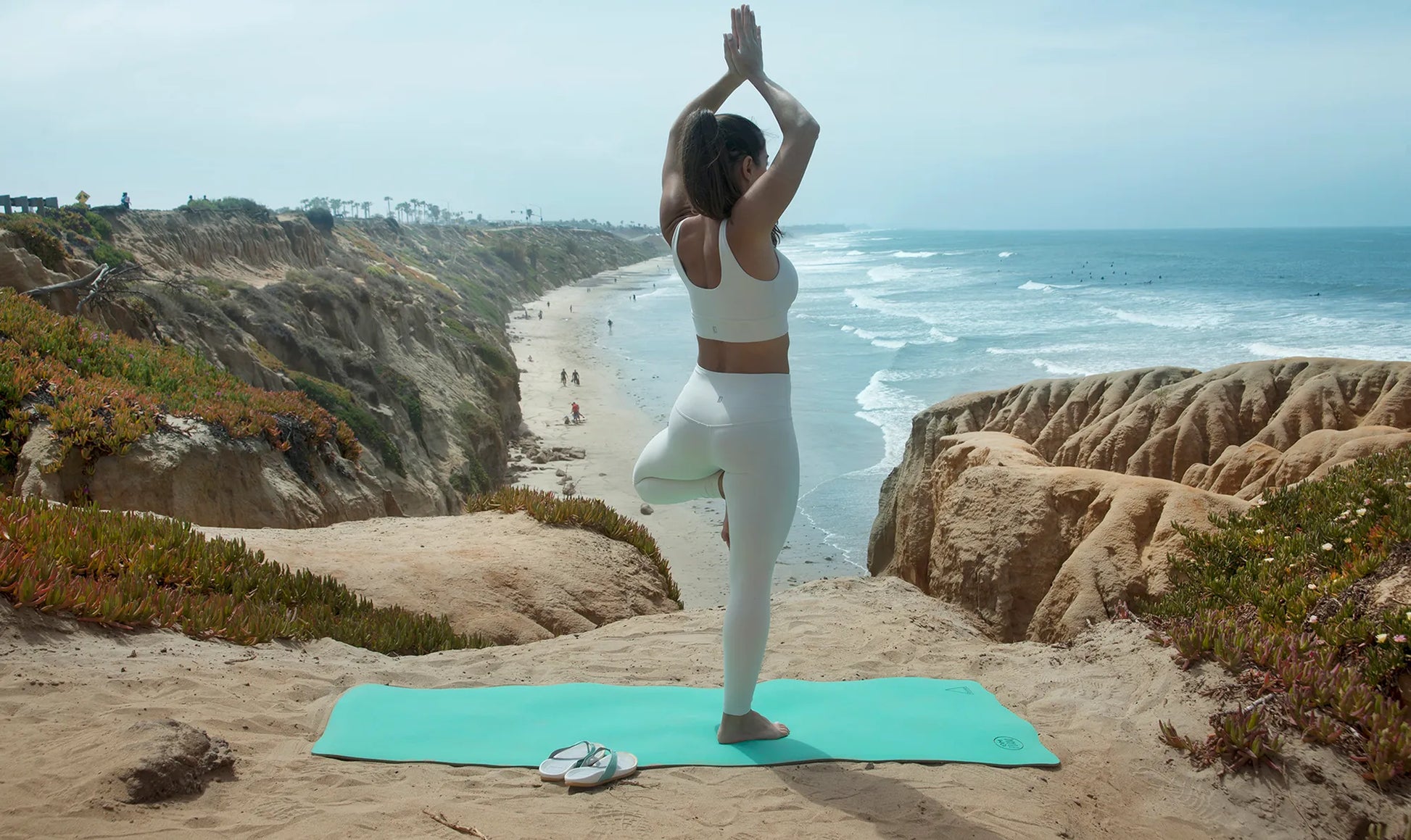 Woman doing a yoga pose on a teal yoga mat on a beach.
