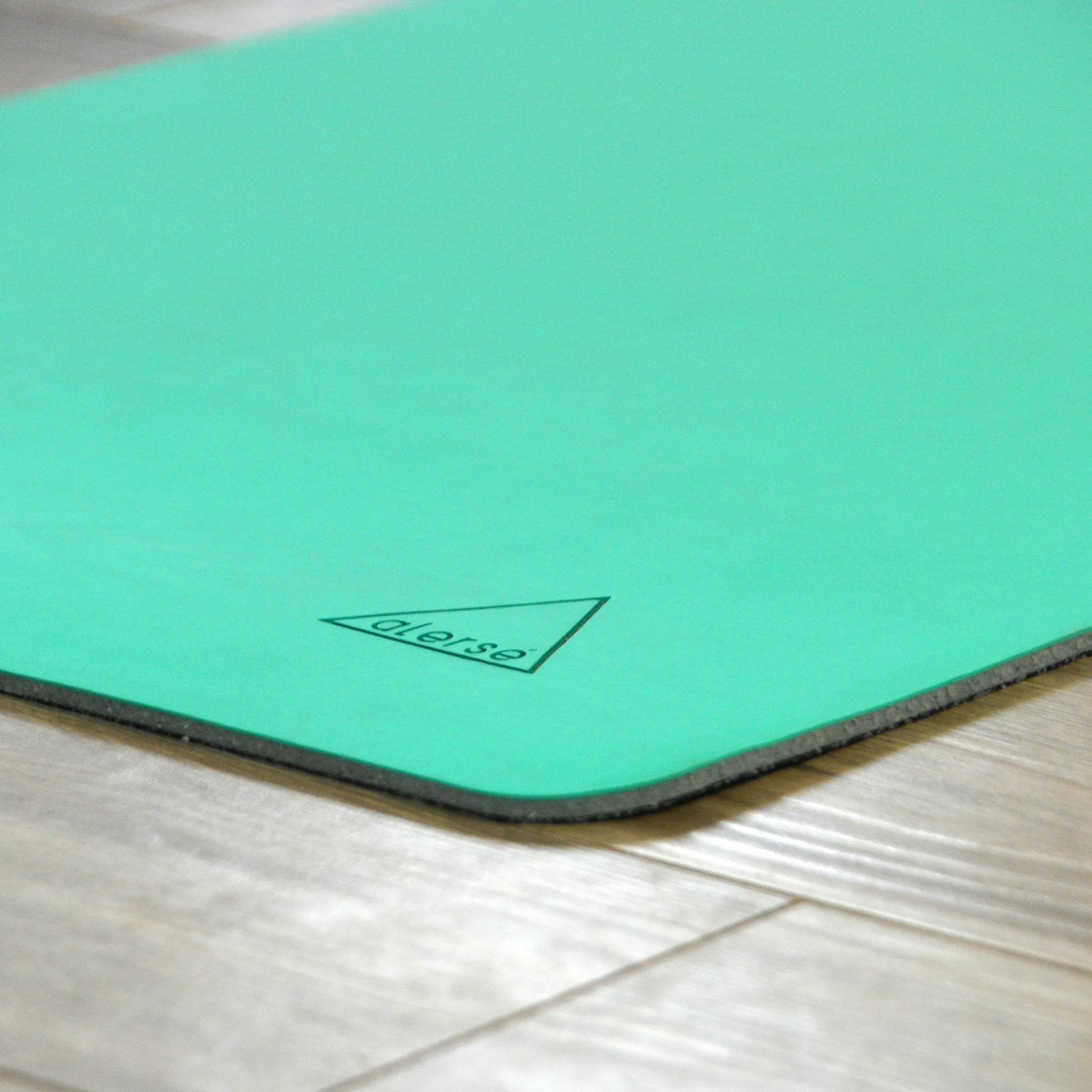 Corner of a teal yoga mat with a Alerse logo on it.