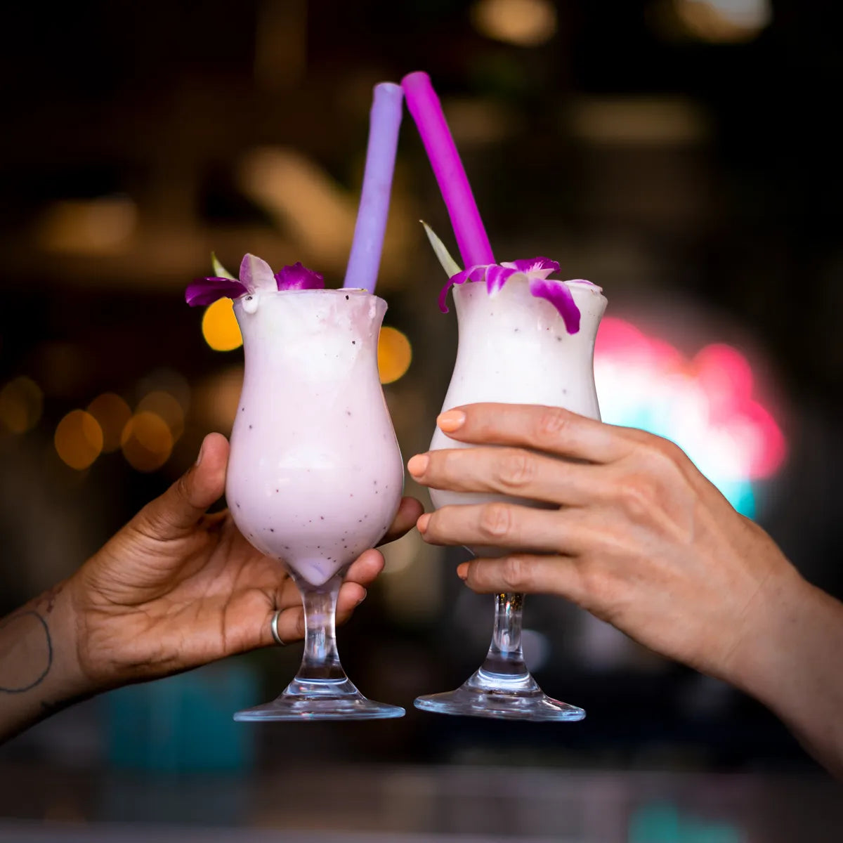 Two glasses with pink and purple straws in them.