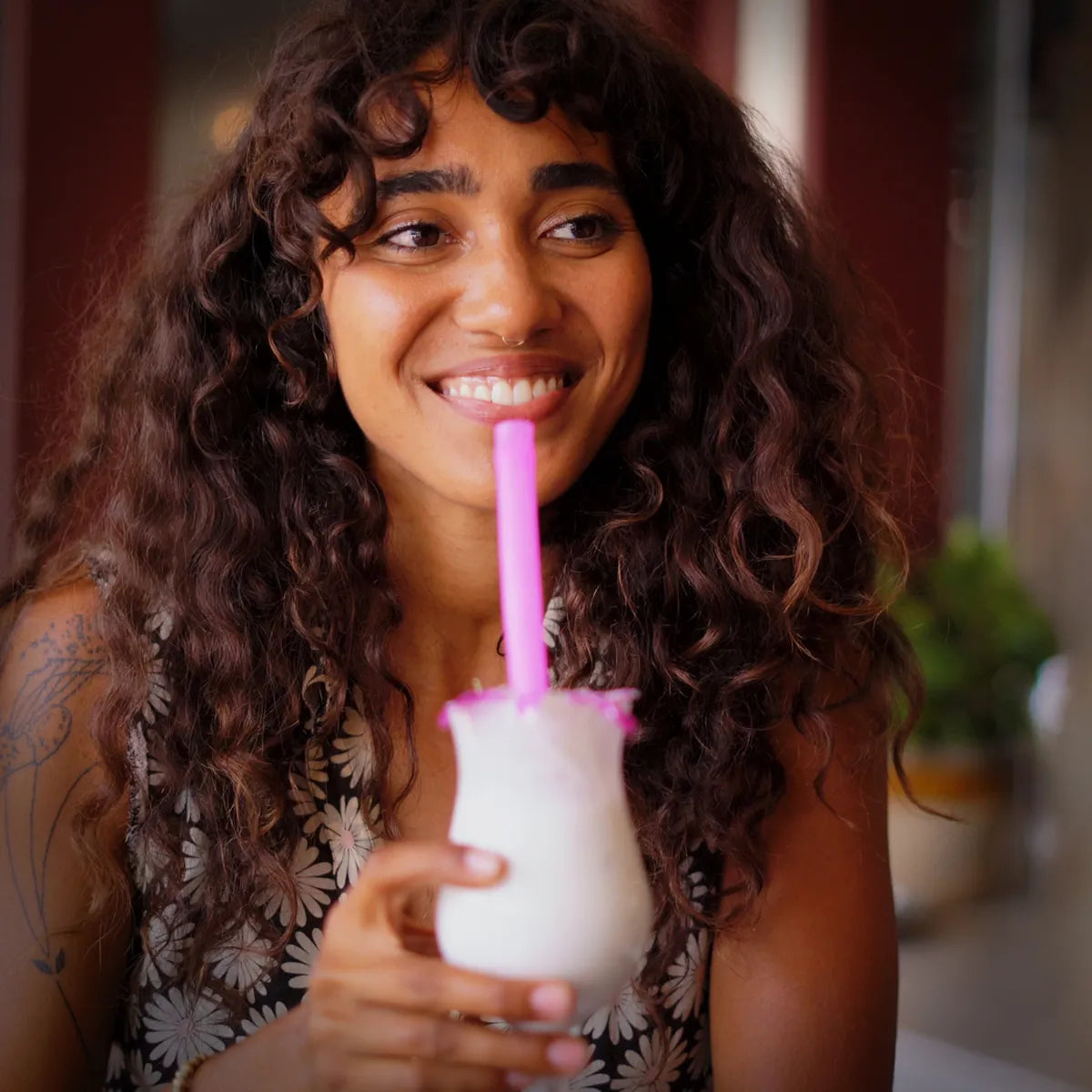 Woman drinking out of a glass using a pink straw.