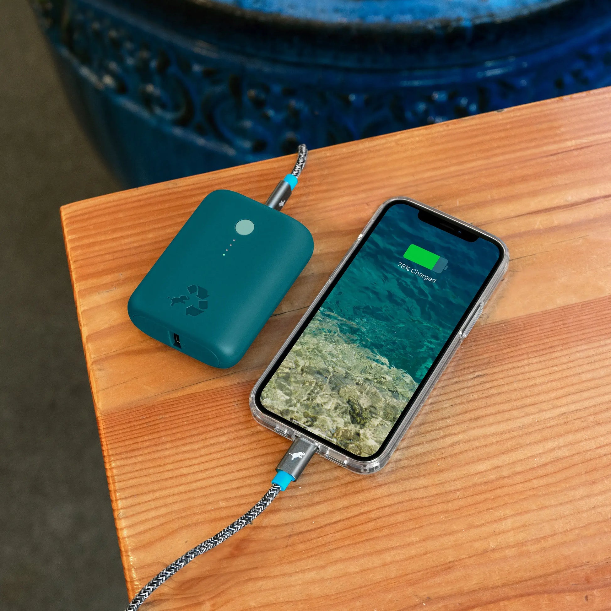 Turquoise portable charger with green button connected to cell phone on a table.