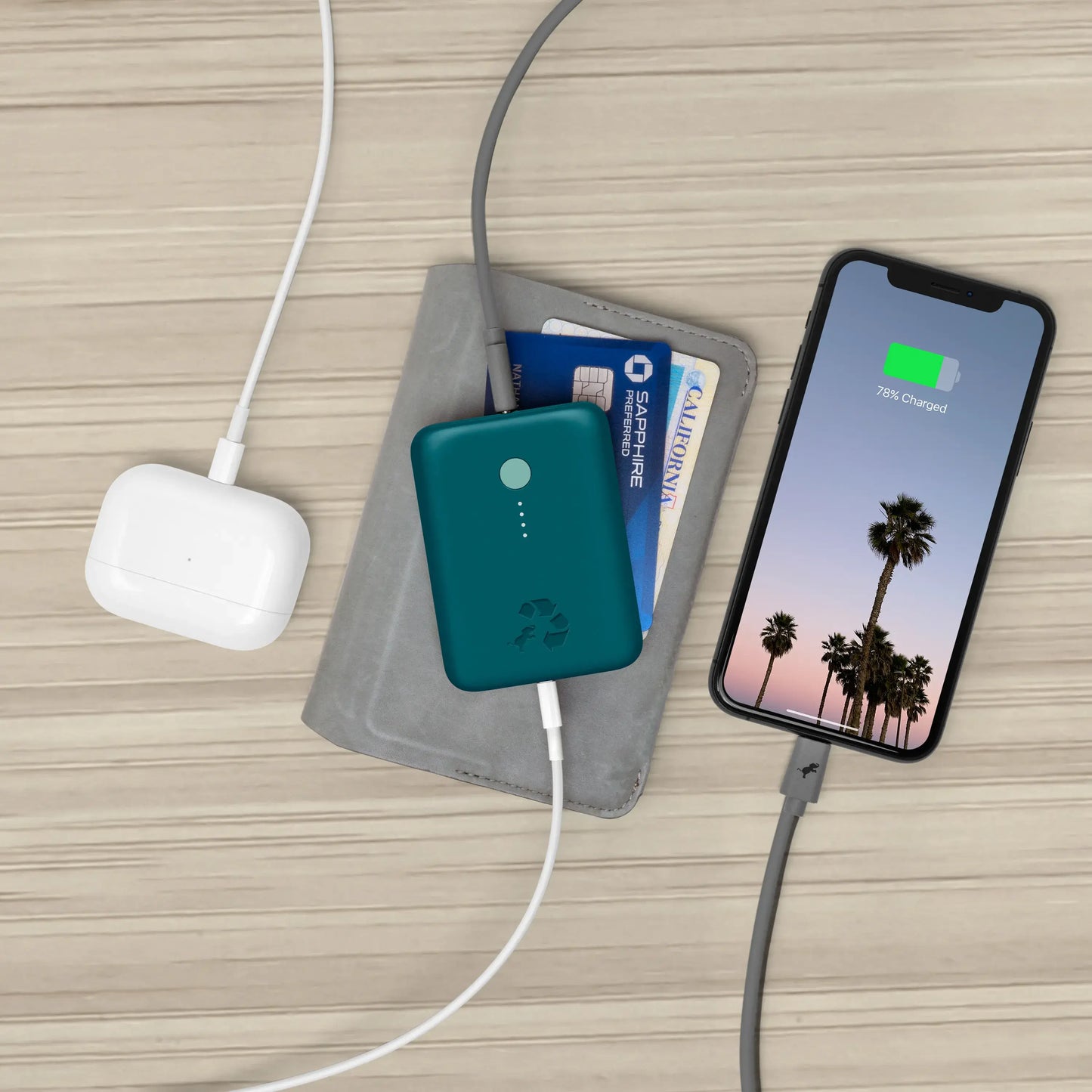 Turquoise portable charger with green button connected to airpods and cell phone.
