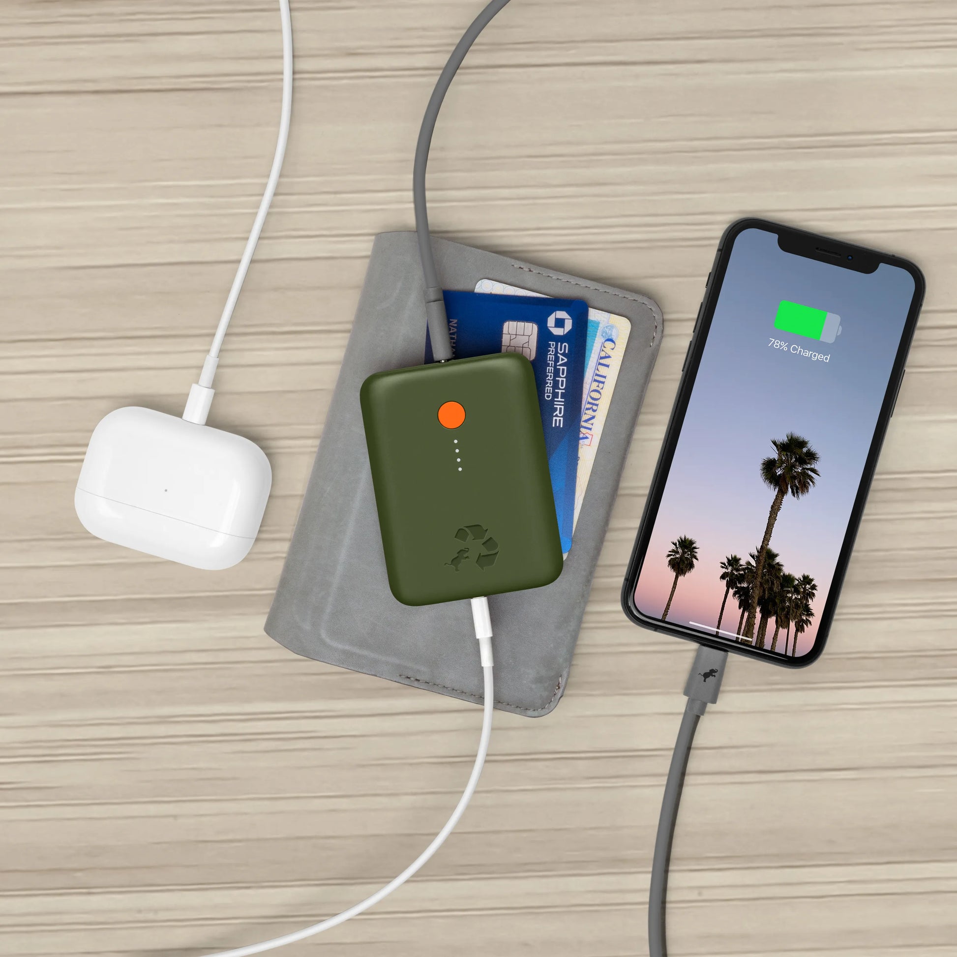 Green portable charger with orange button connected to airpods and cell phone.