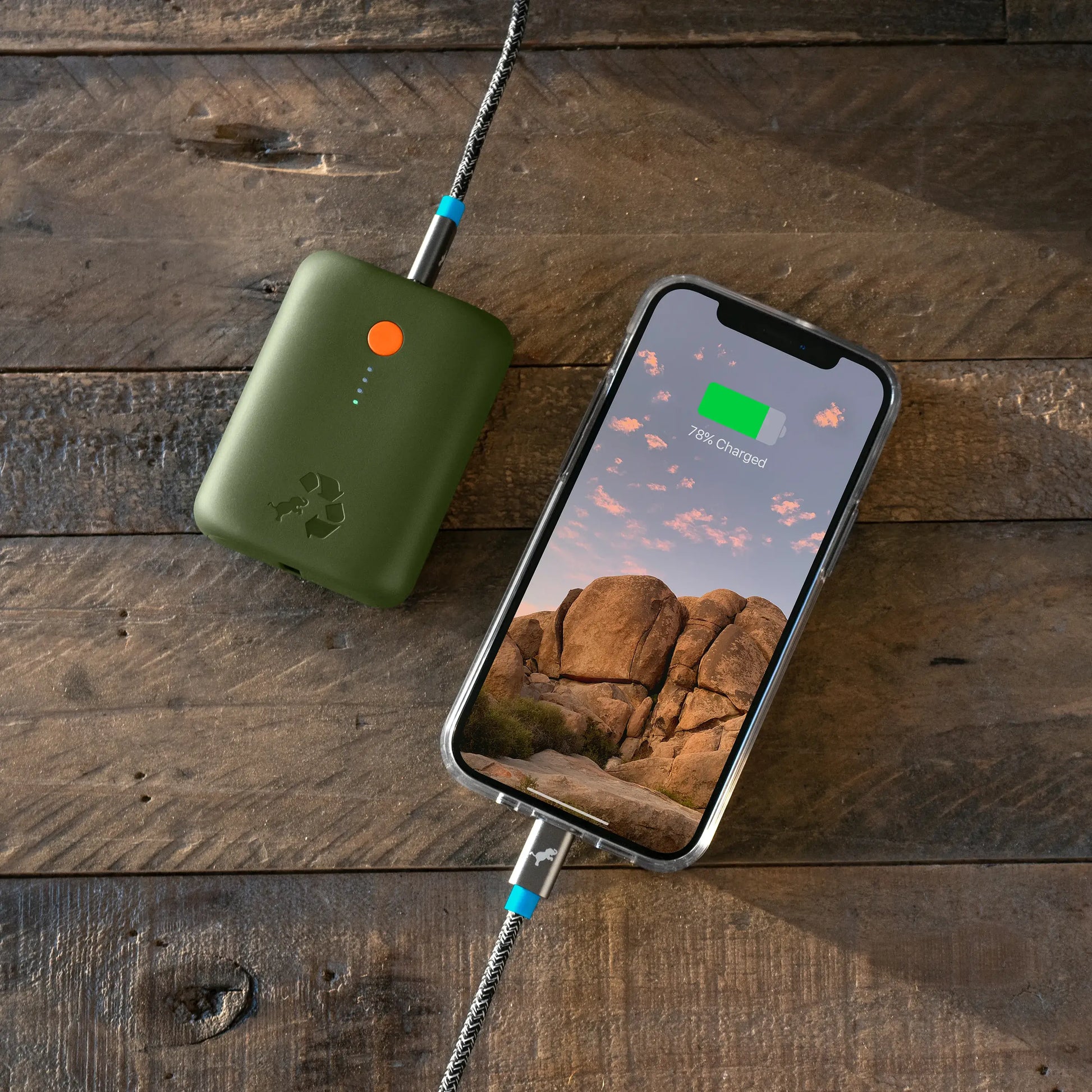 Green portable charger with orange button connected to cell phone on table.