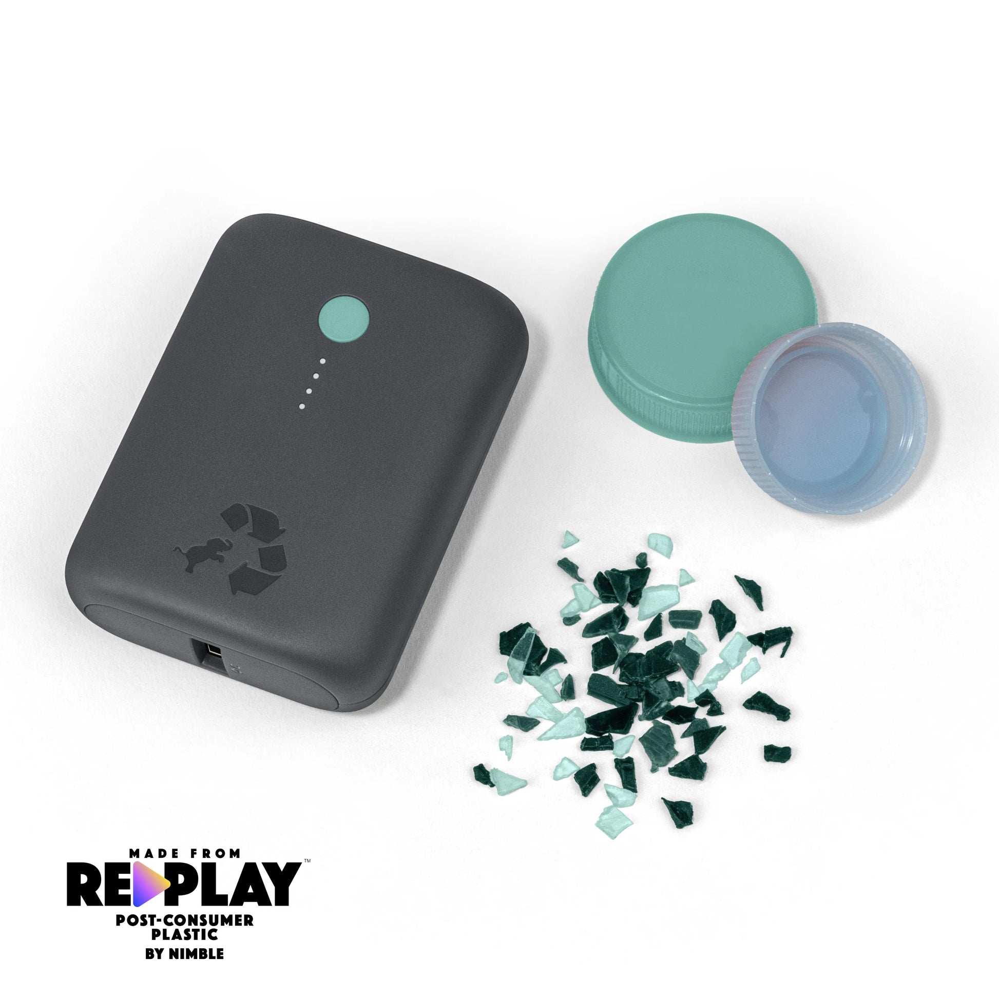 Charcoal portable charger with green button next to bottle caps and shredded plastic.