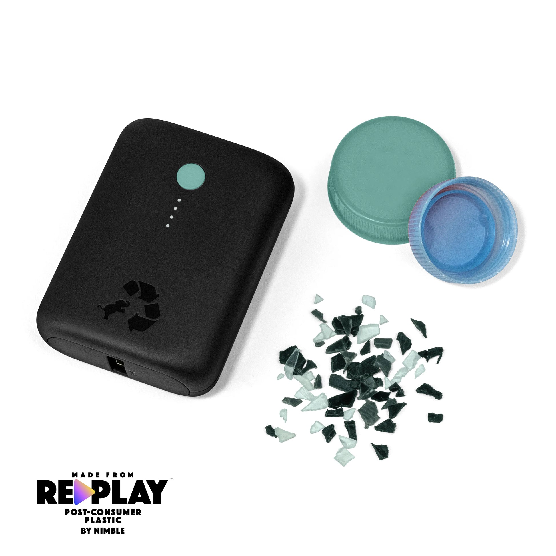 Black portable charger with green button next to bottle caps and shredded plastic.