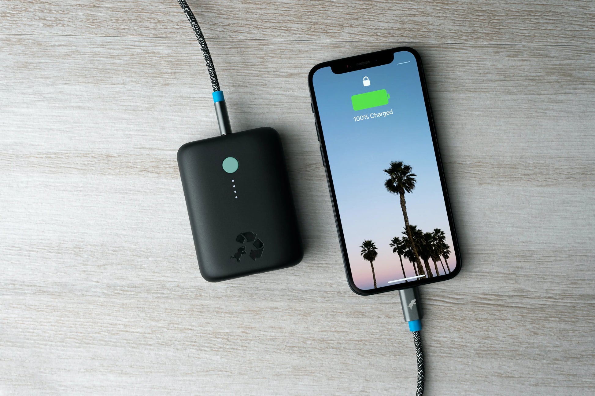 Black portable charger with green button connected to cell phone on table.