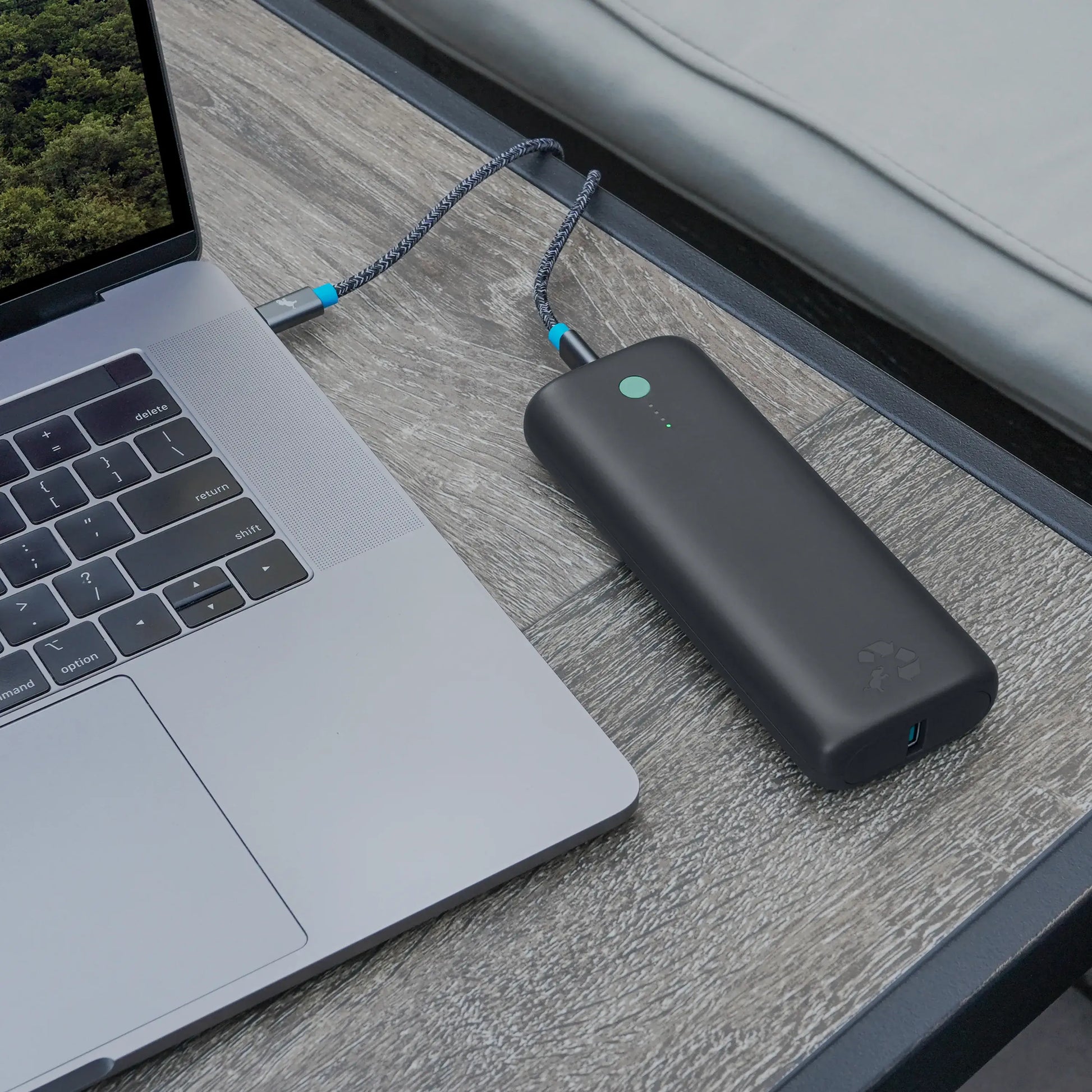 Large dark gray portable charger with green button connected to laptop.