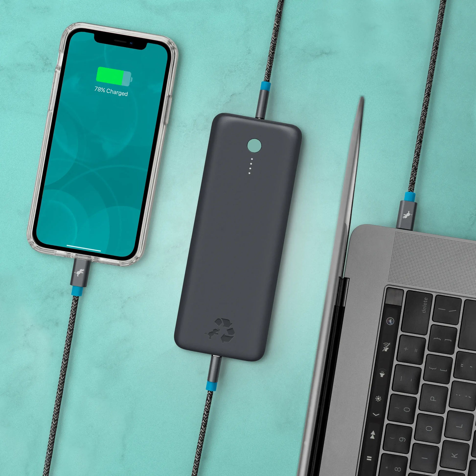 Large dark gray portable charger with green button connected to cell phone and laptop.