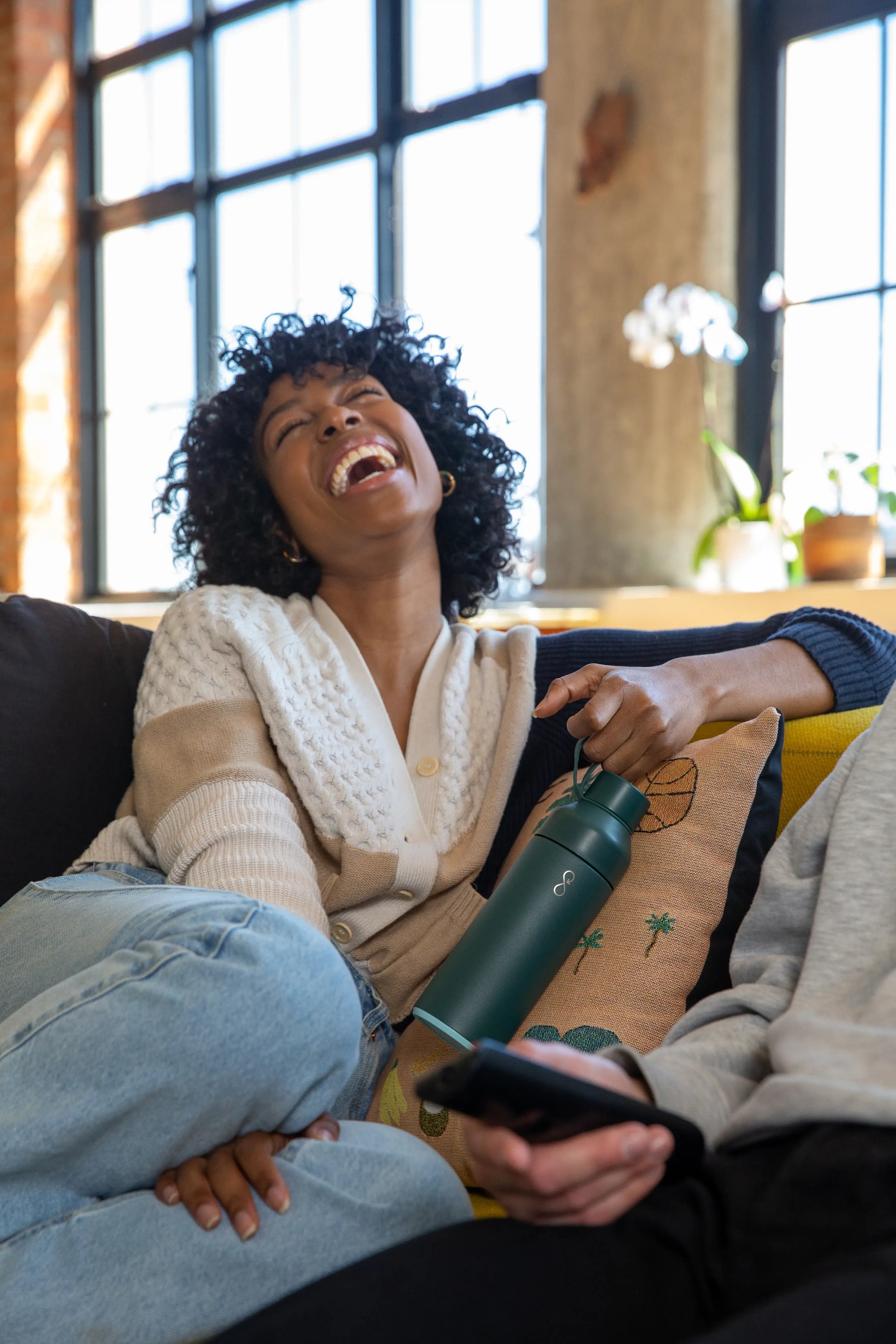 Woman laughing on a couch holding a green water bottle.