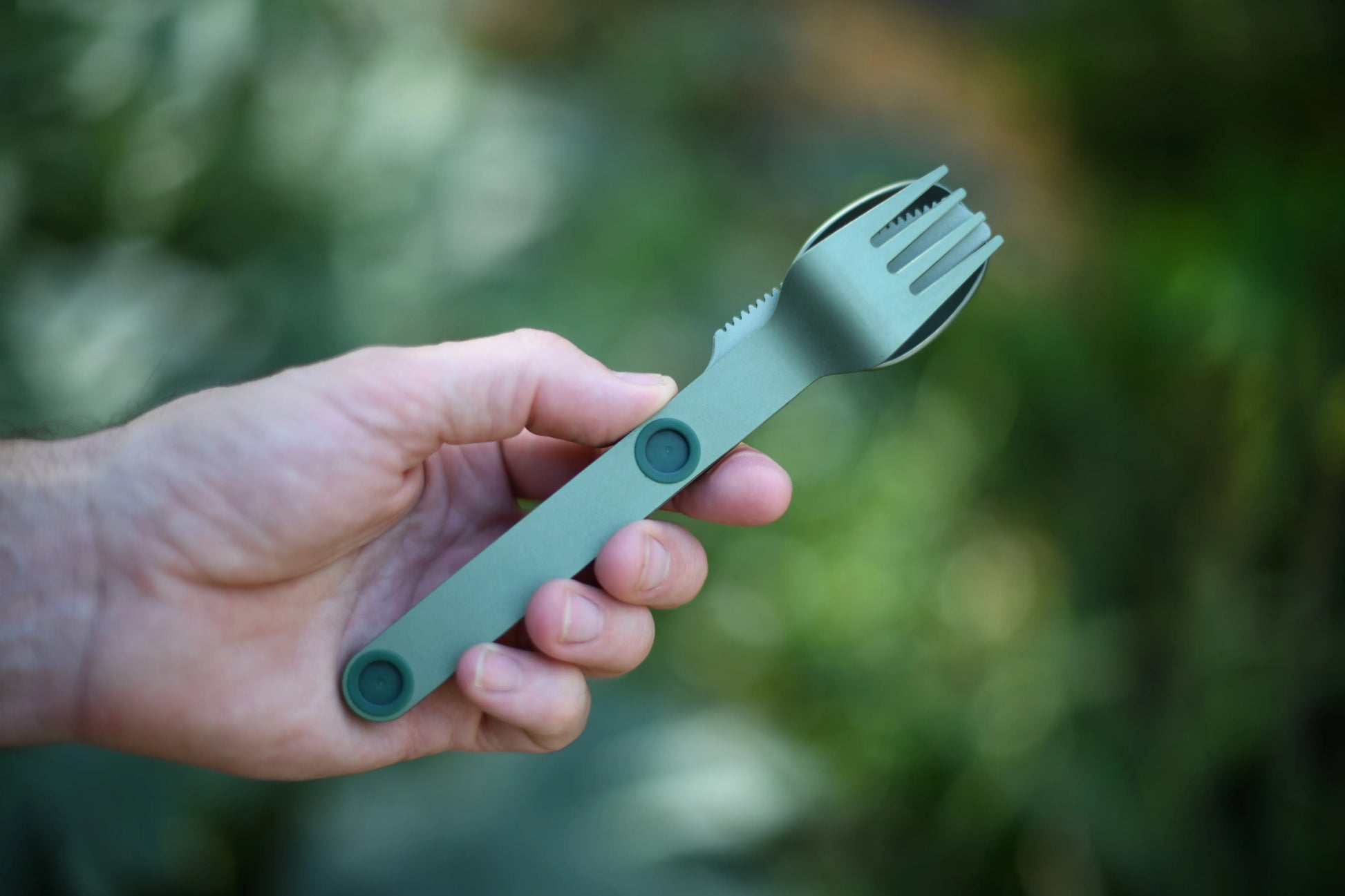 Hand holding green fork, knife and spoon connected.