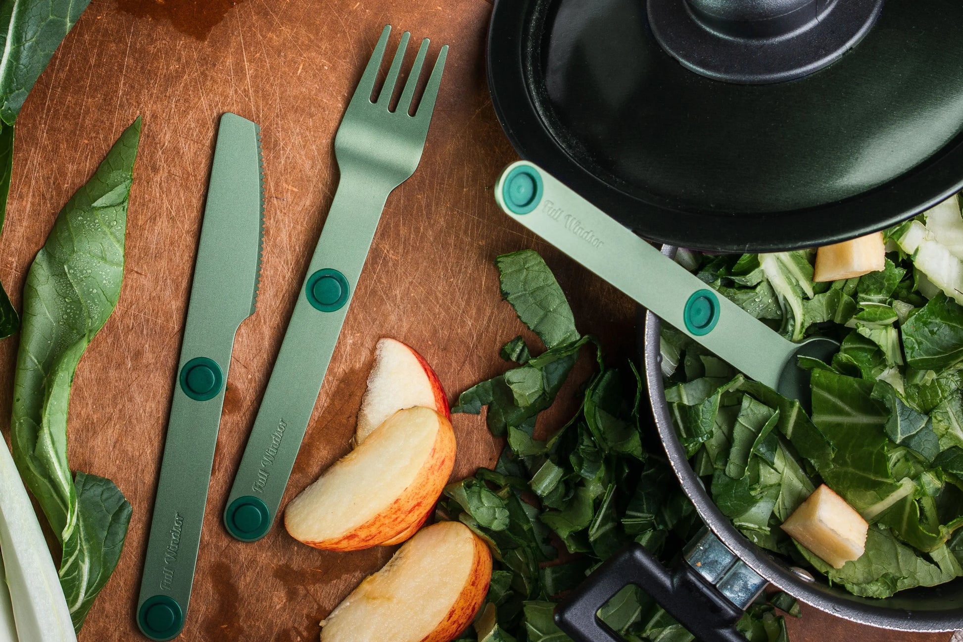 Green fork, knife and spoon with salad and apple slices.