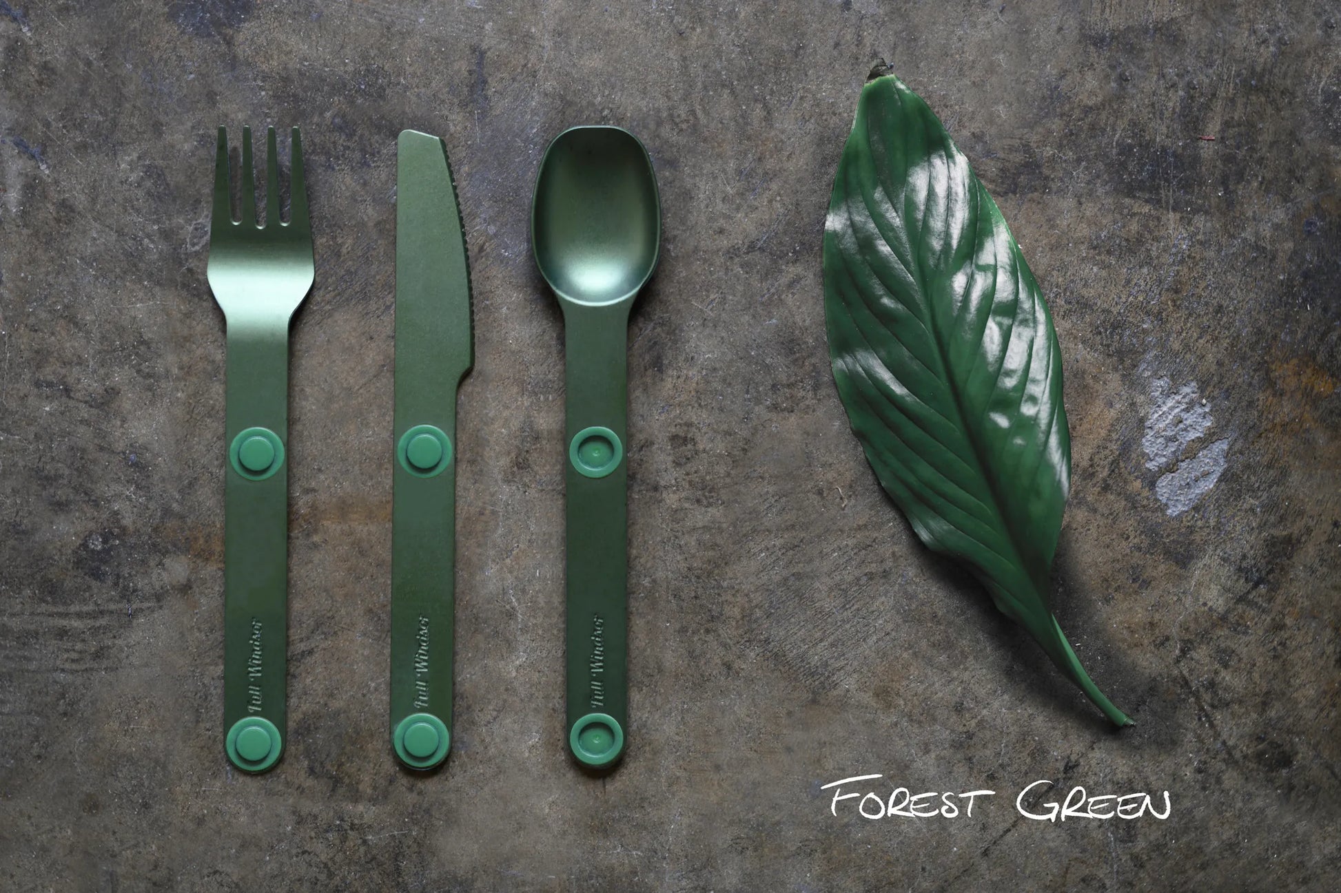 Green fork, knife and spoon next to a green leaf.