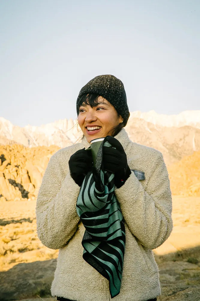 Woman outside holding a mini towel with teal and black lines.