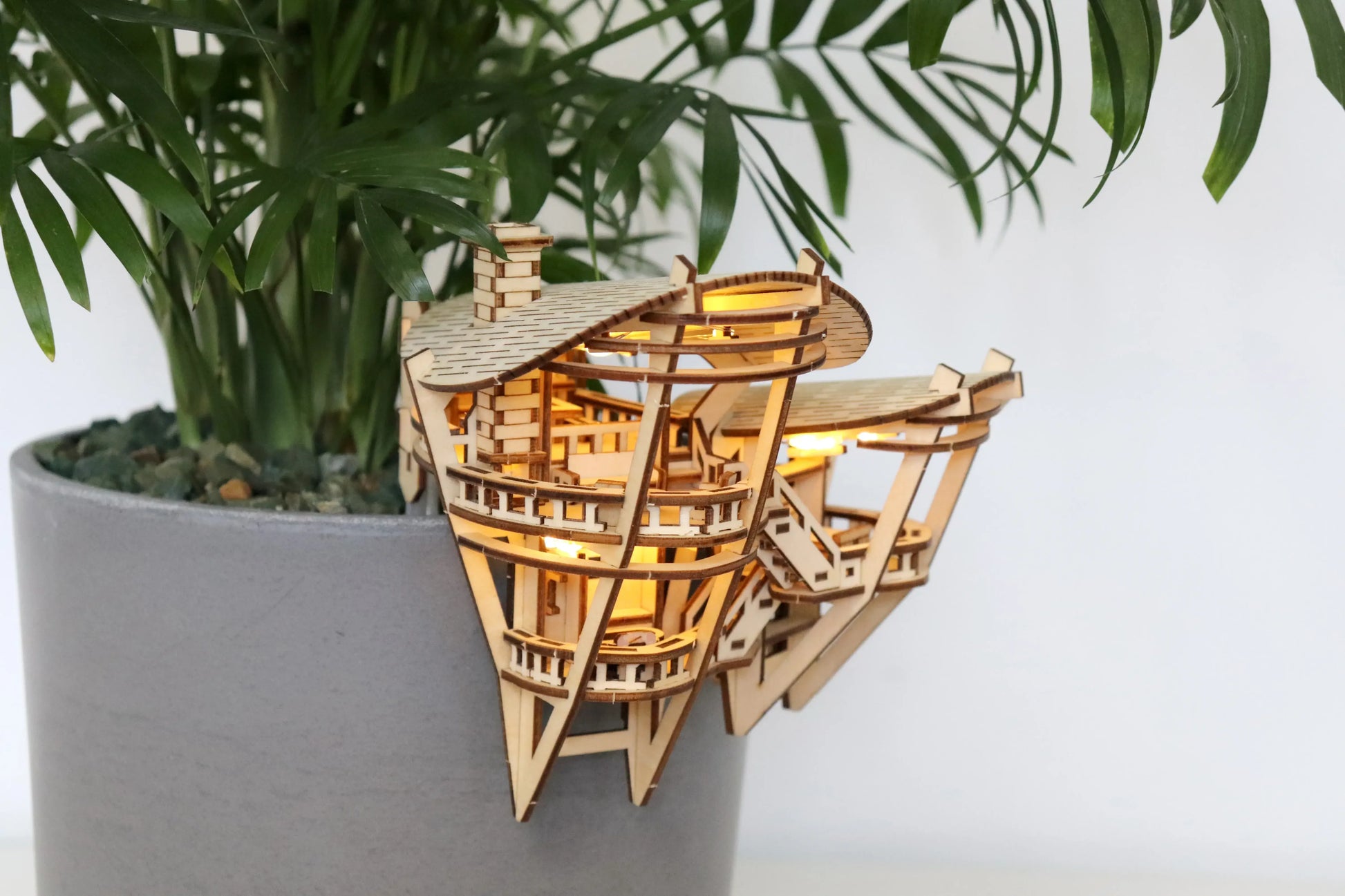 Small wooden treehouse with lights hanging on side of pot.