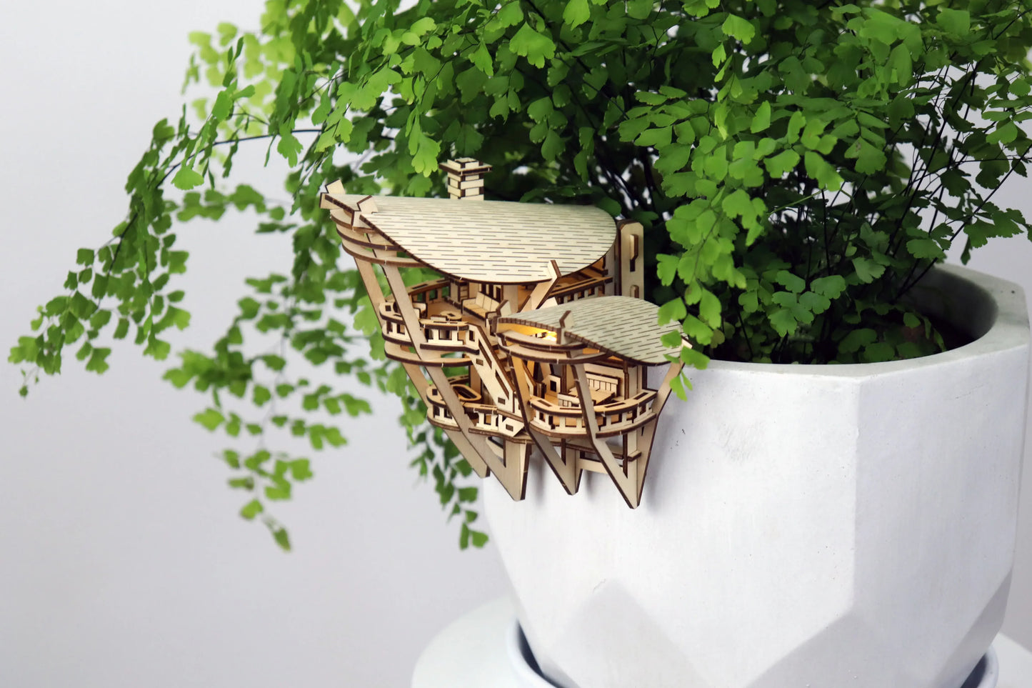 Small wooden treehouse hanging on side of white pot.