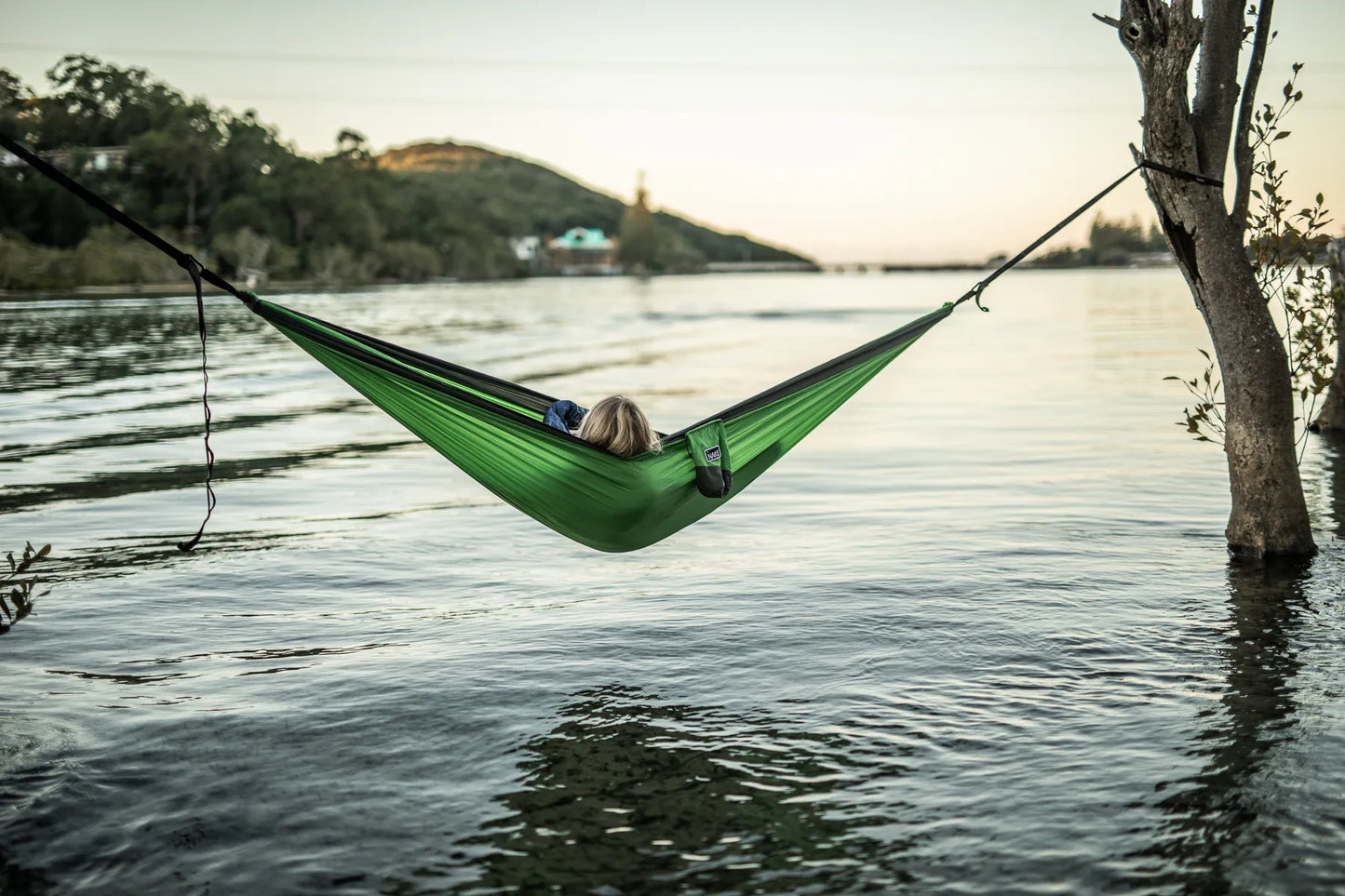 Woman laying in a green and gray hammock over the water.