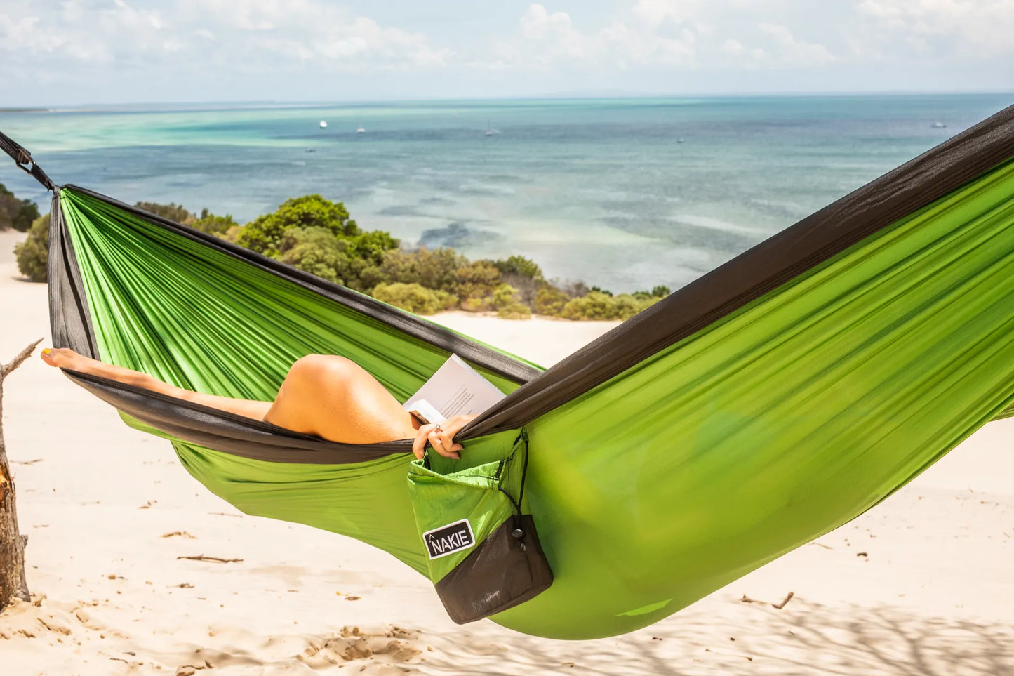 Woman on the beach laying in a green and gray hammock.
