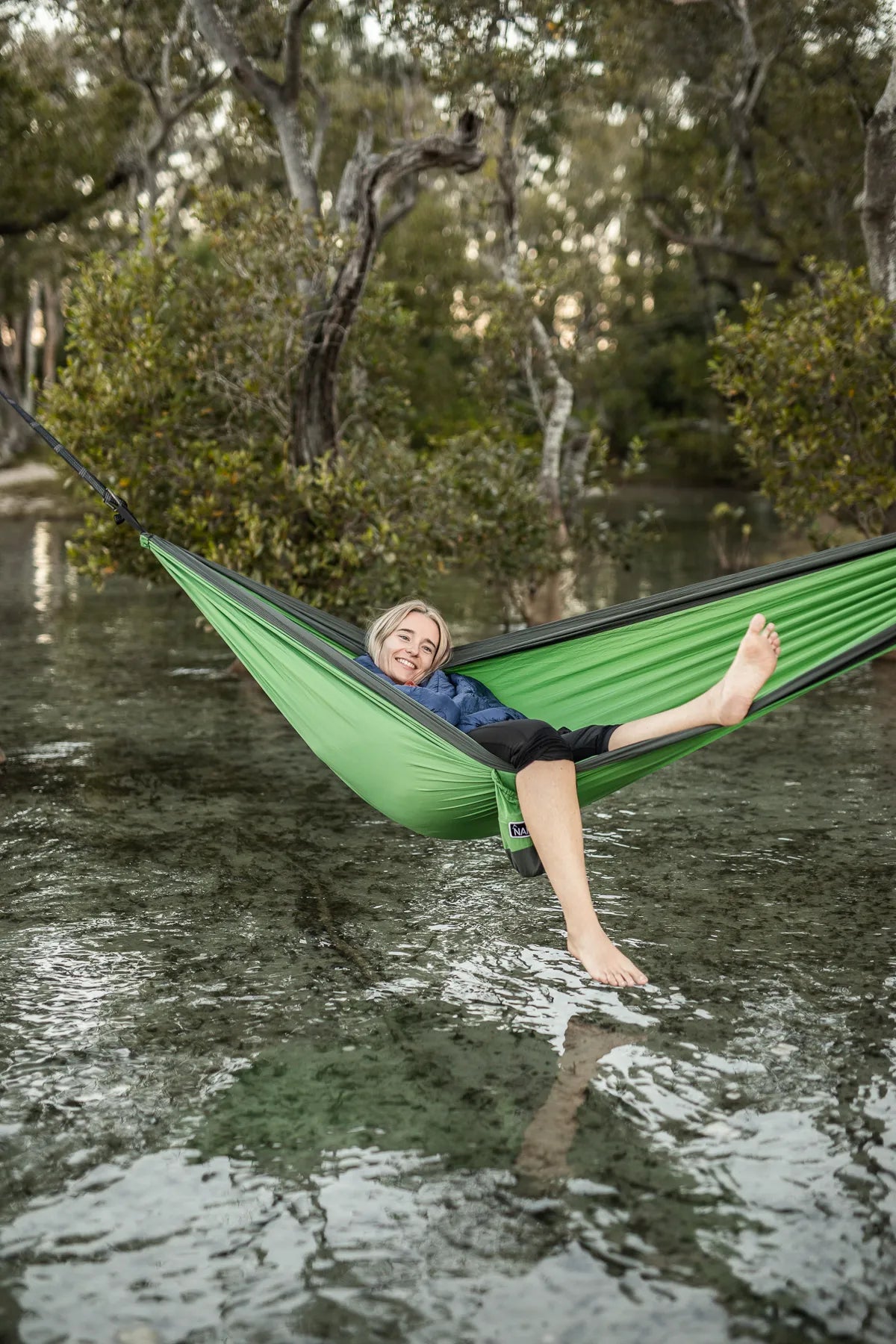 Woman sitting in a green and gray hammock over the water.