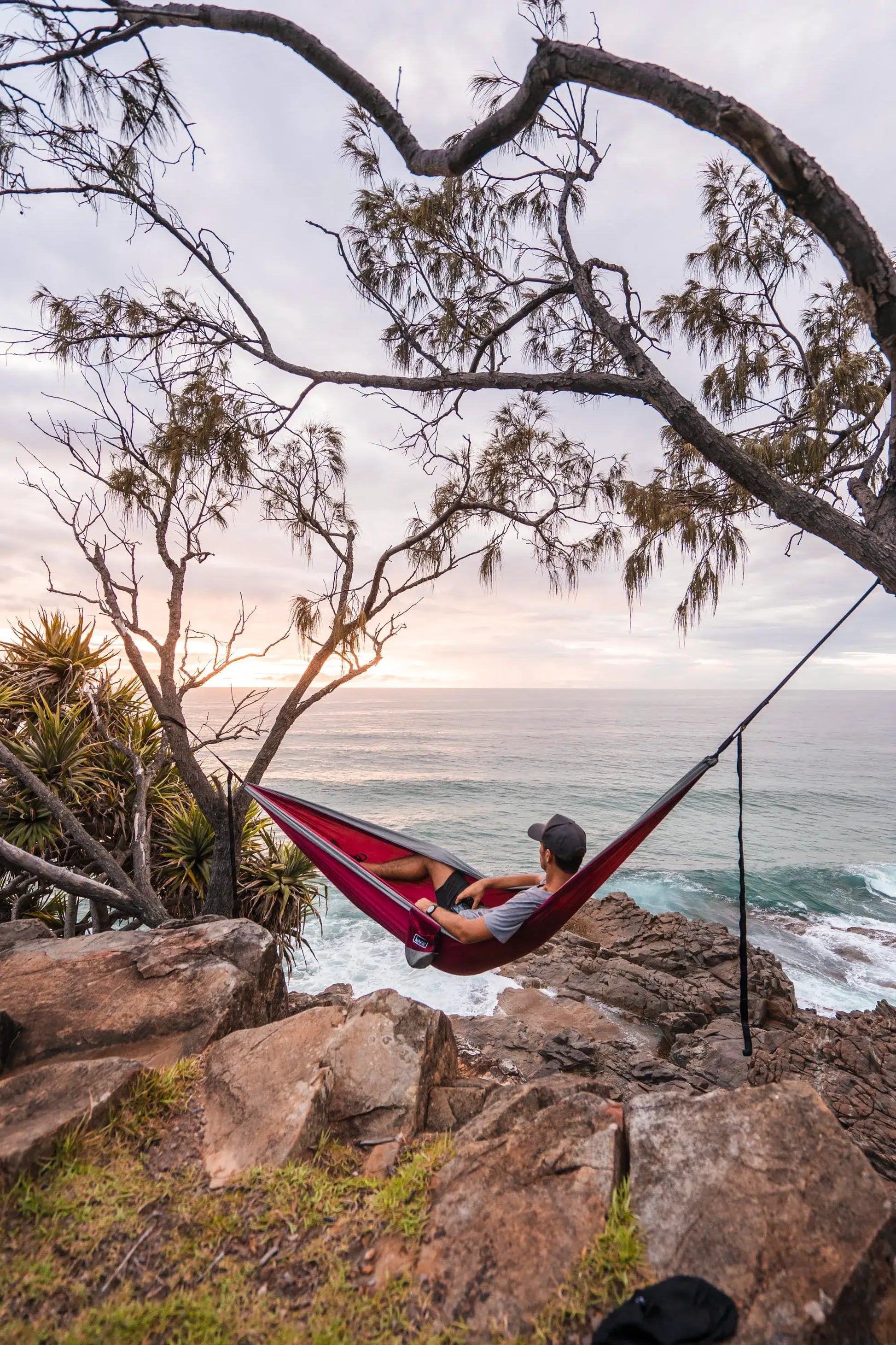 Man sitting in a red and gray hammock on a cliff.