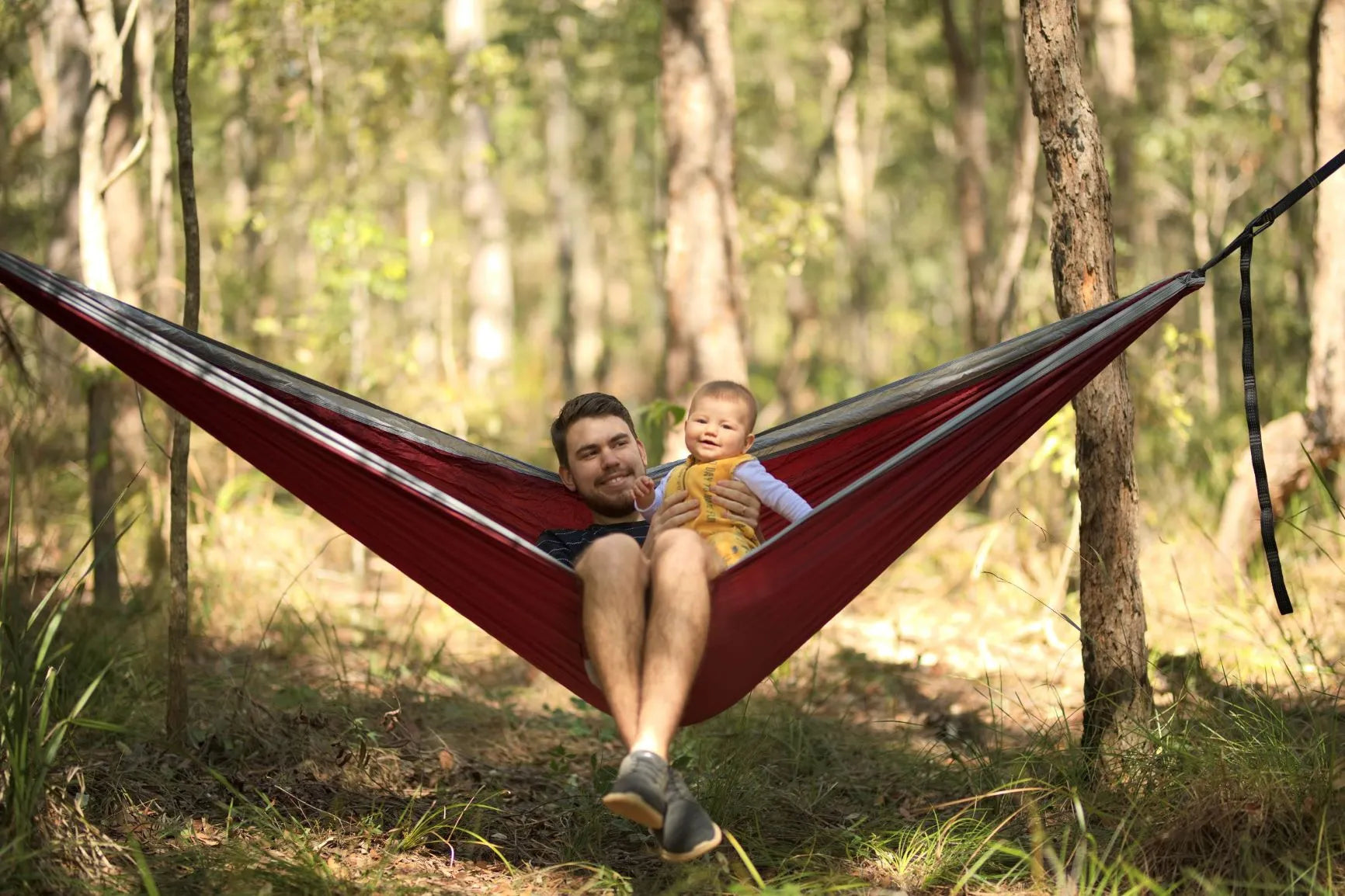 Father and baby outside sitting in a red and gray hammock.