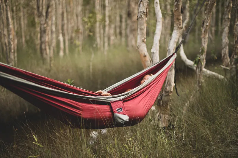 Woman sleeping in a red and gray hammock in the woods.
