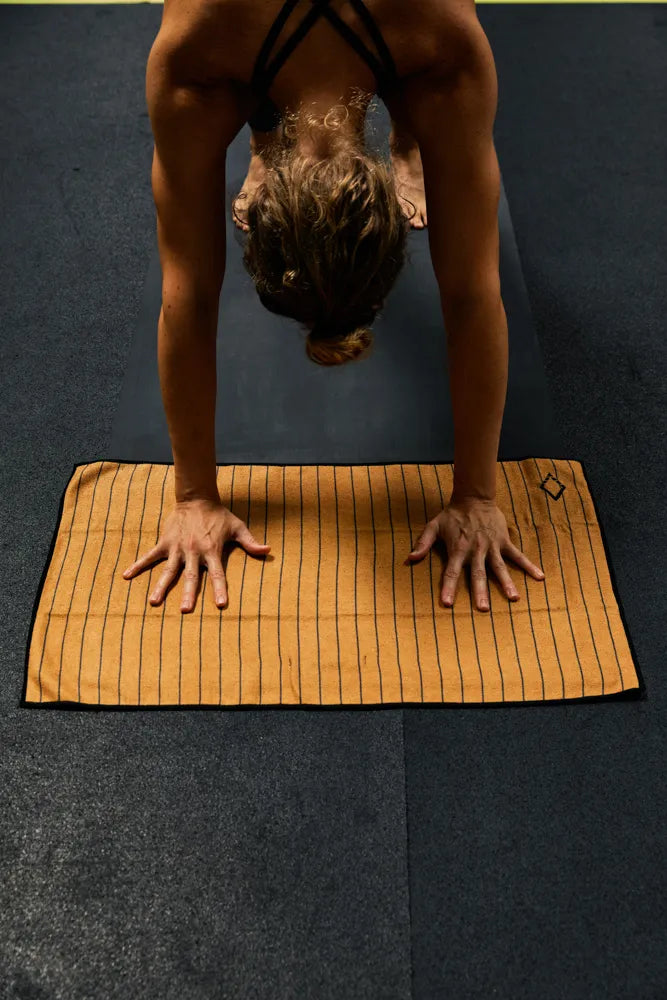 Woman exercising on a small orange hand towel with black pinstripes.