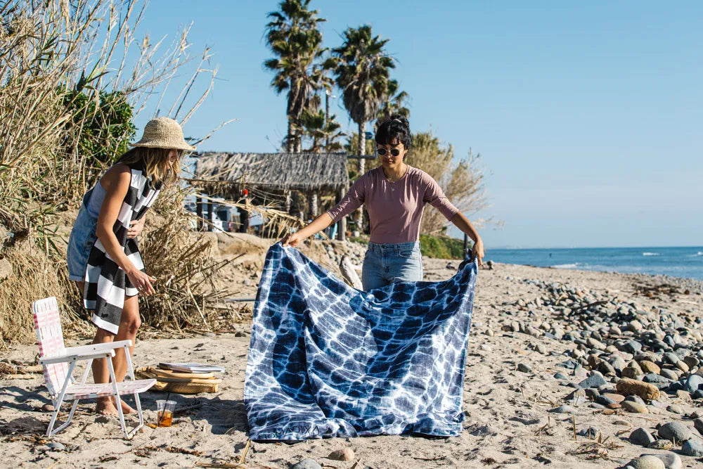 Two girls laying out a blue and white beach blanket.