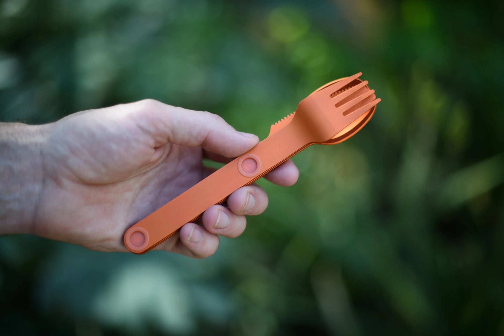 Hand holding an orange fork, spoon and knife connected.