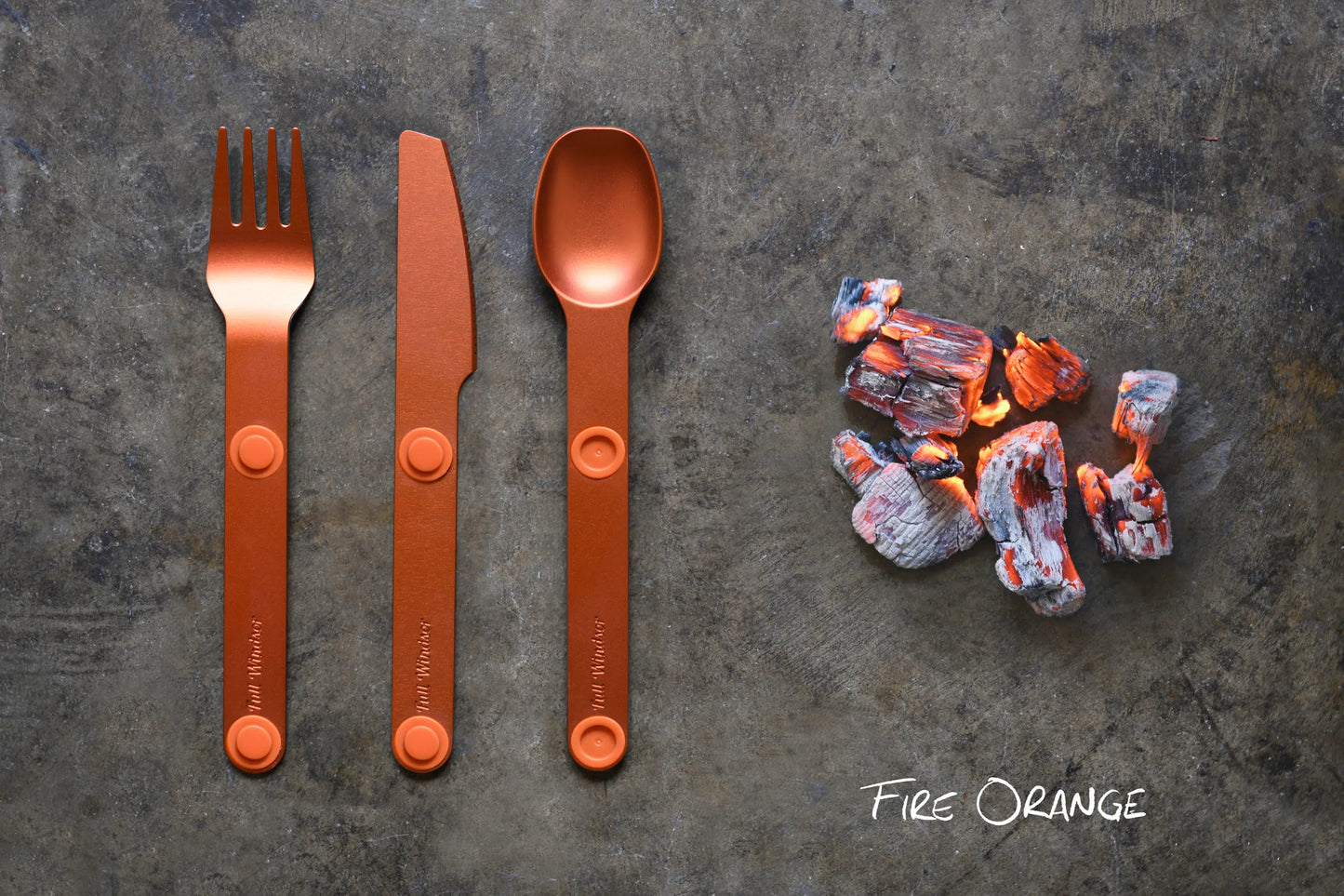 Orange fork, spoon and knife next to hot coals.