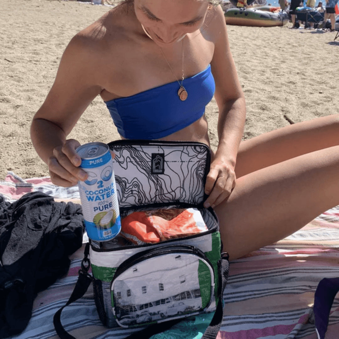 Woman on the beach taking a can out of a cooler bag.