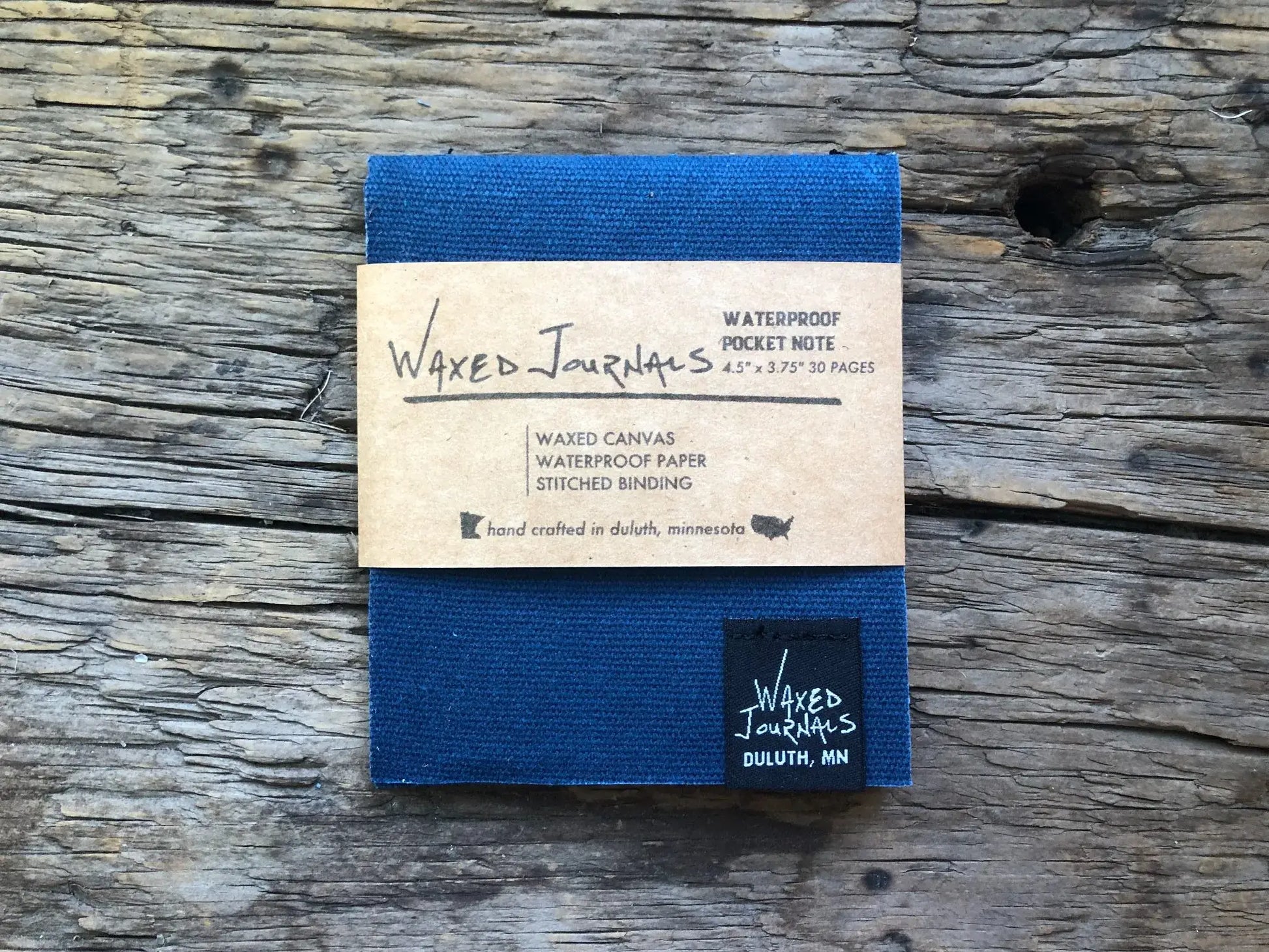 Blue waxed journal notepad with packaging on wood.