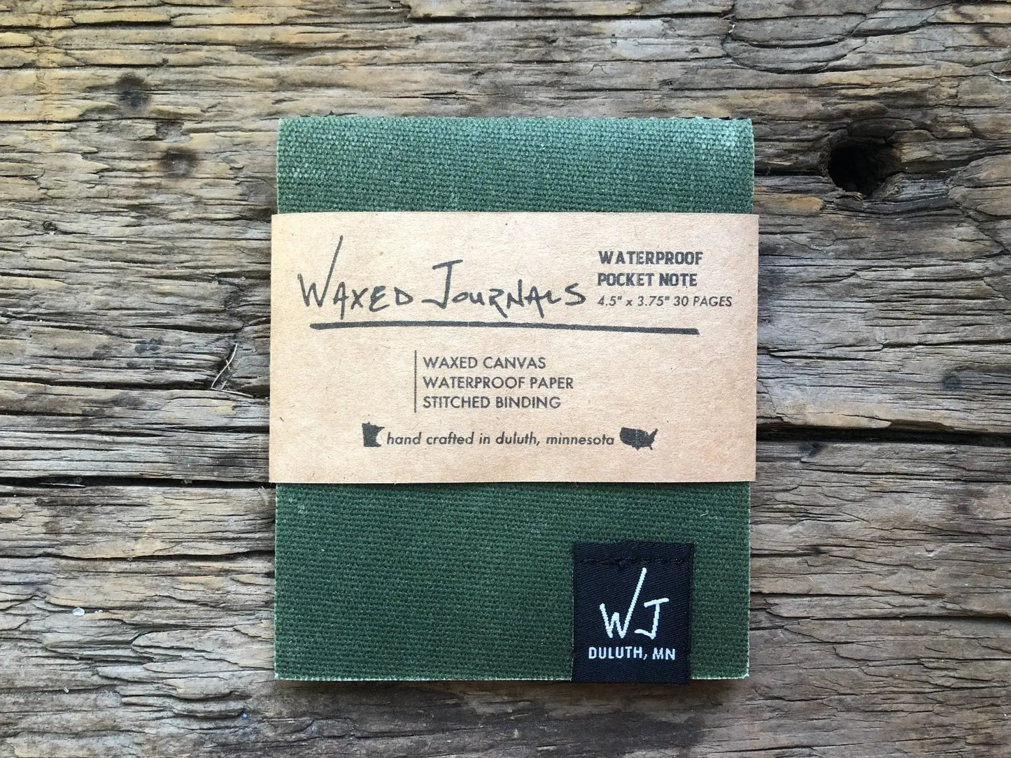 Green waxed journal notepad in packaging on wood.