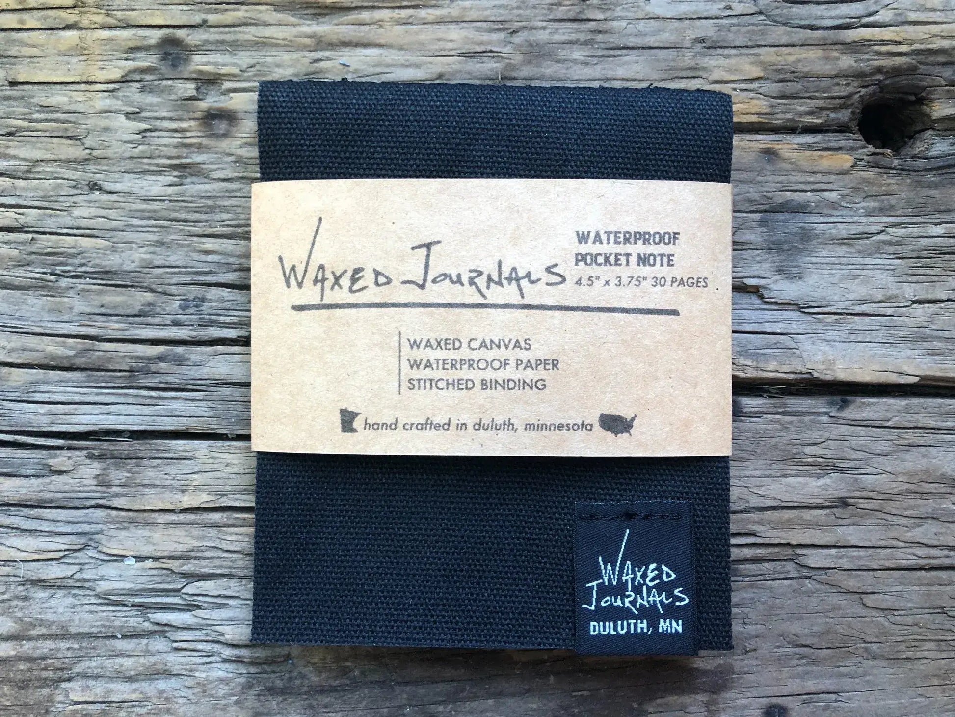 Black waxed journal notepad in packaging on wood.