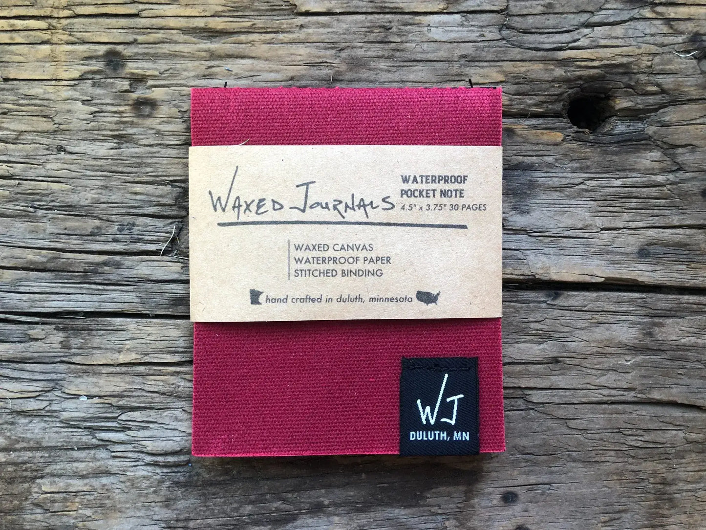 Red waxed journal notepad in packaging on wood.
