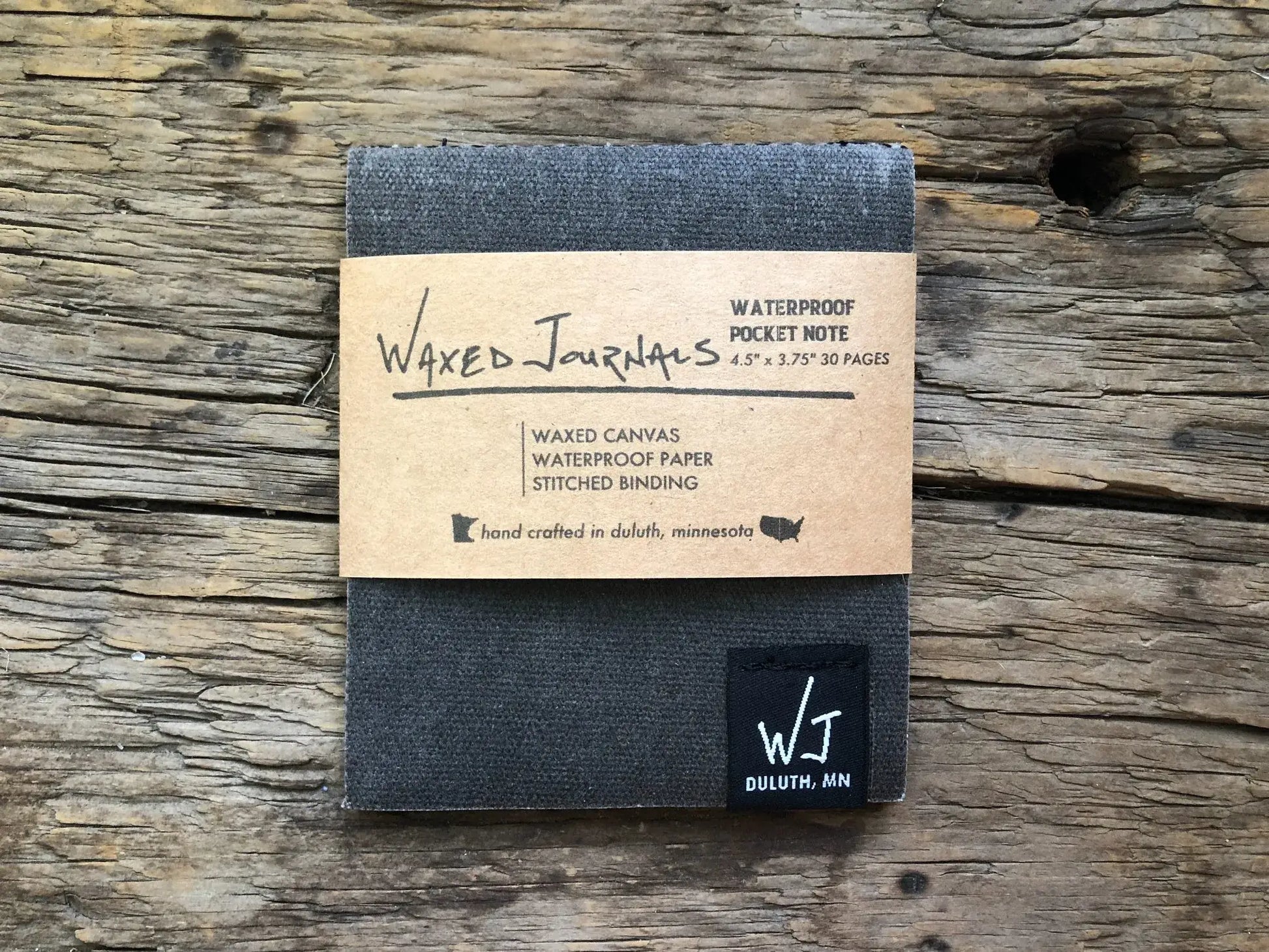 Gray waxed journal notepad with packaging on wood.