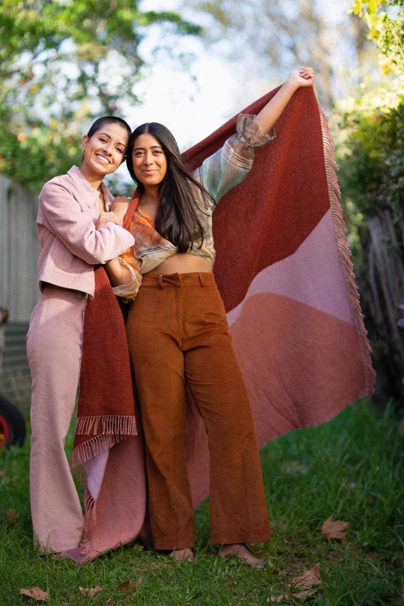 Two women showing a red and pink wool blanket.