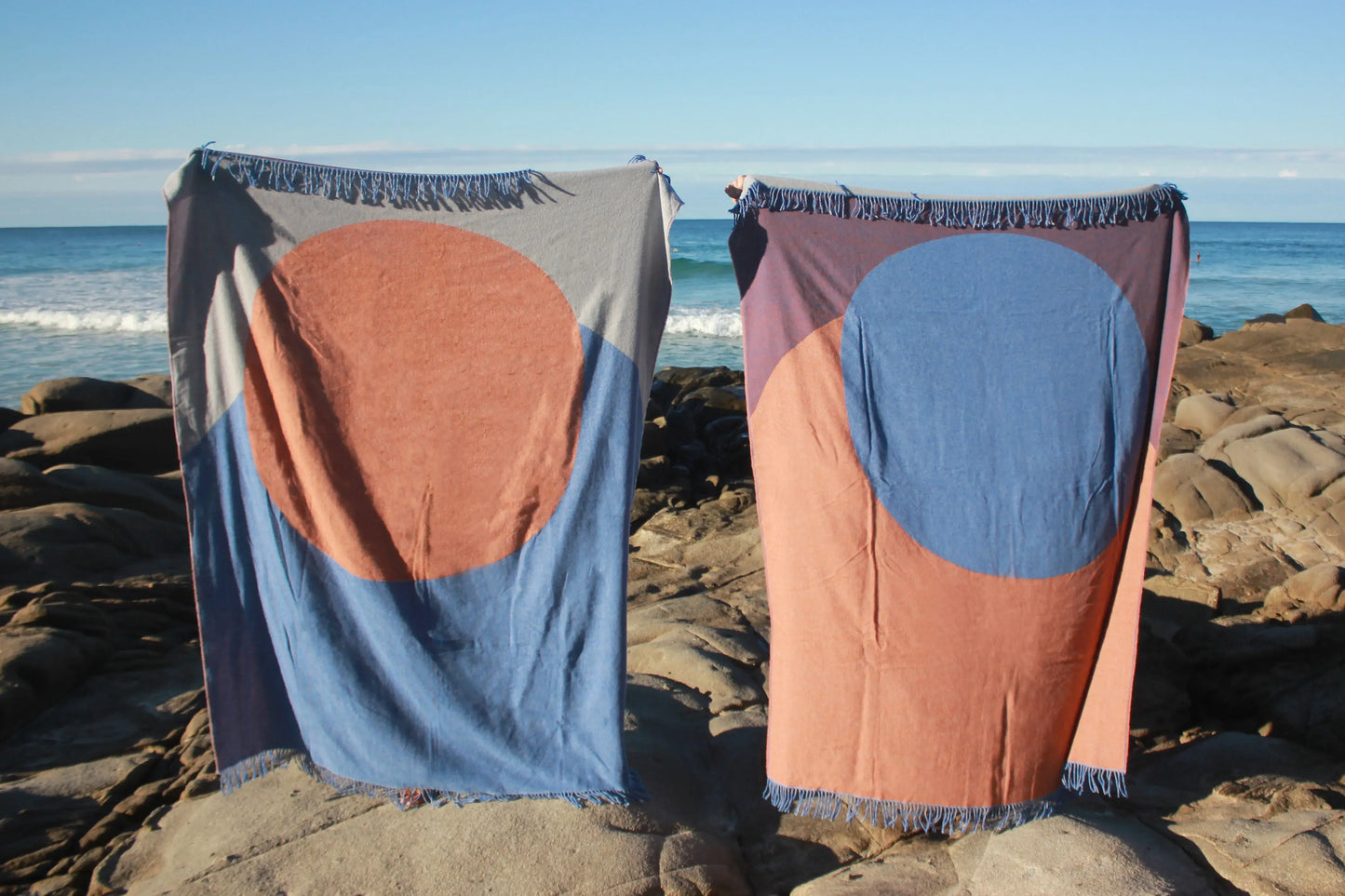 Two wool blankets being held up on a beach.