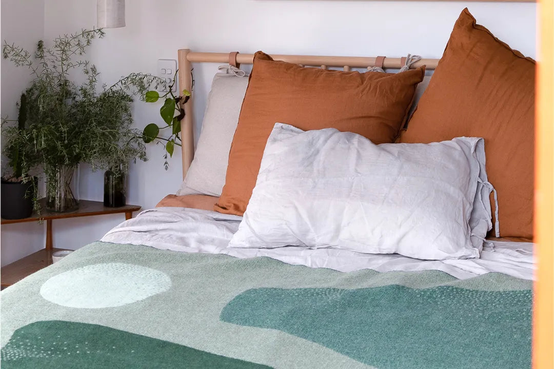 Wool blanket with different shapes and shades of green on a bed.