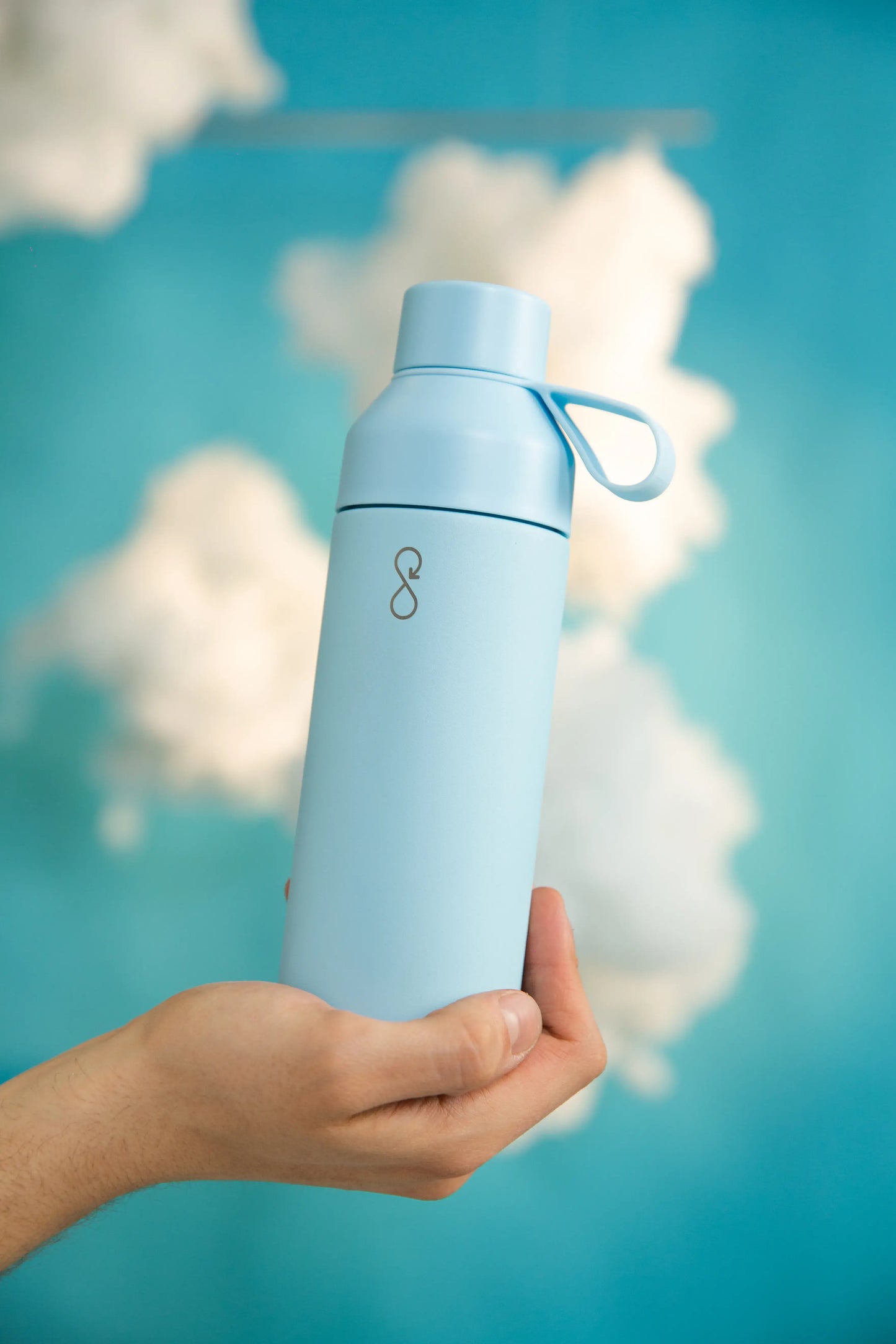 Hand holding a blue water bottle in front of clouds.