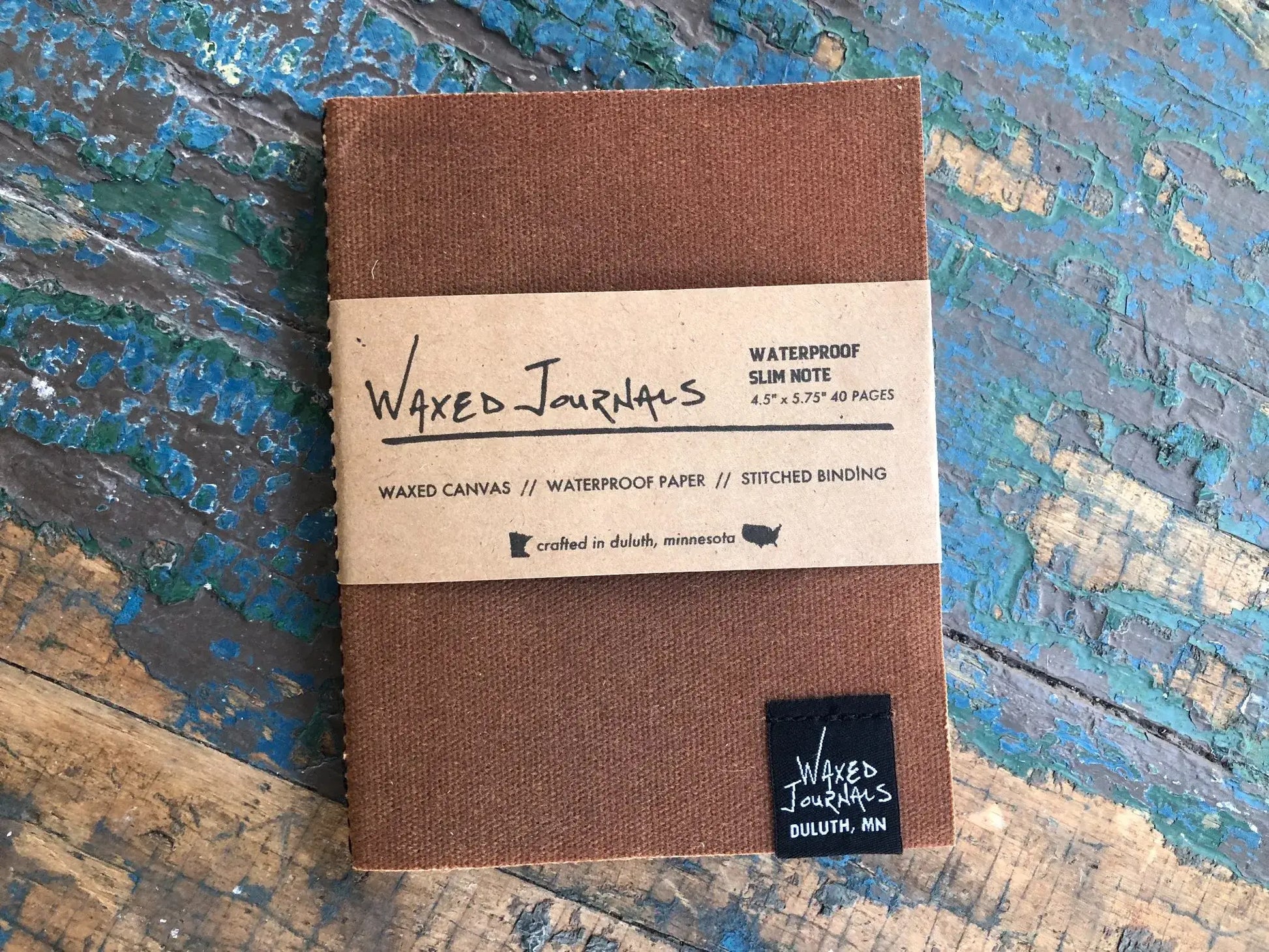 Brown waxed journal notebook in packaging on blue wood table.